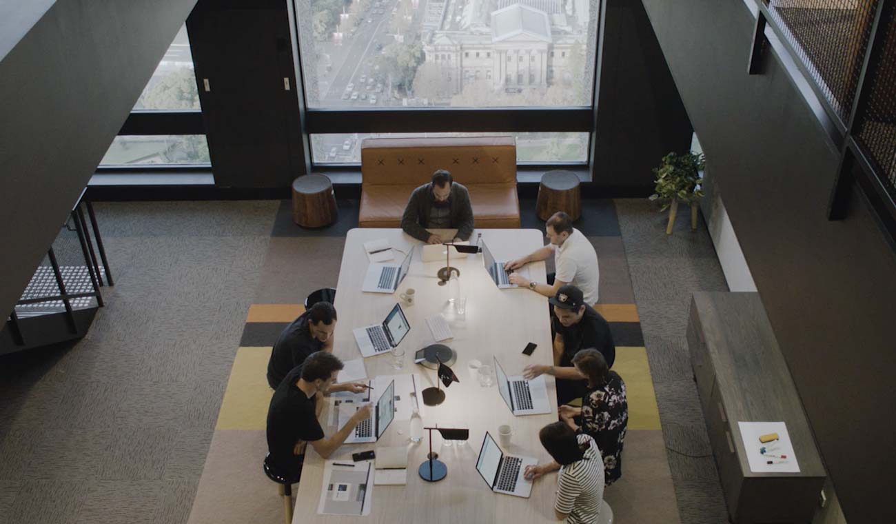 An image of a group of people sitting around a conference table working on laptops.