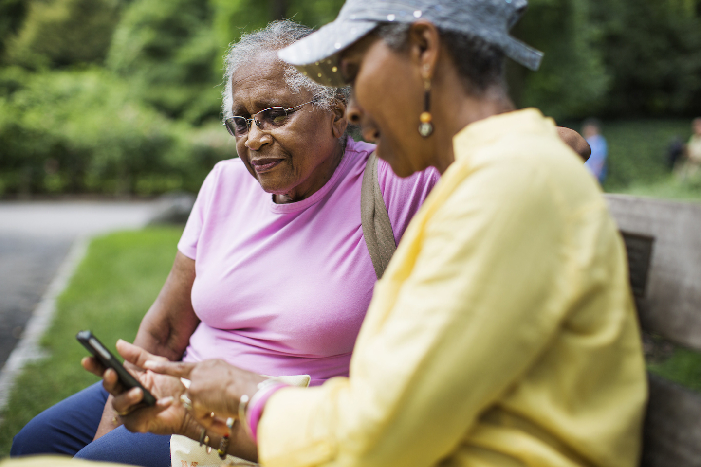 Woman holds and points at her iPhone, and shows another woman photos on her mobile device.