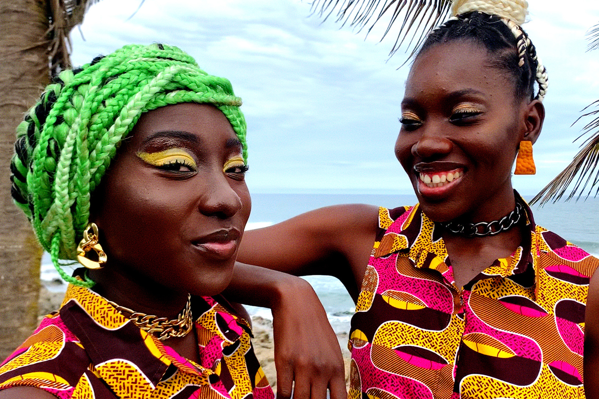 Zwei Frauen in gleich bedruckten Kleidern posieren und lächeln am Strand.