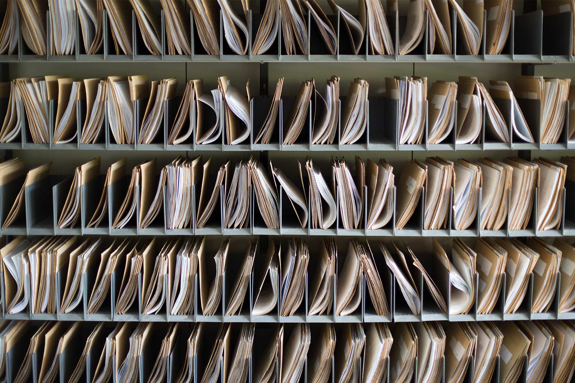 Prateleiras de documentos em papel em pastas organizadas em compartimentos.
