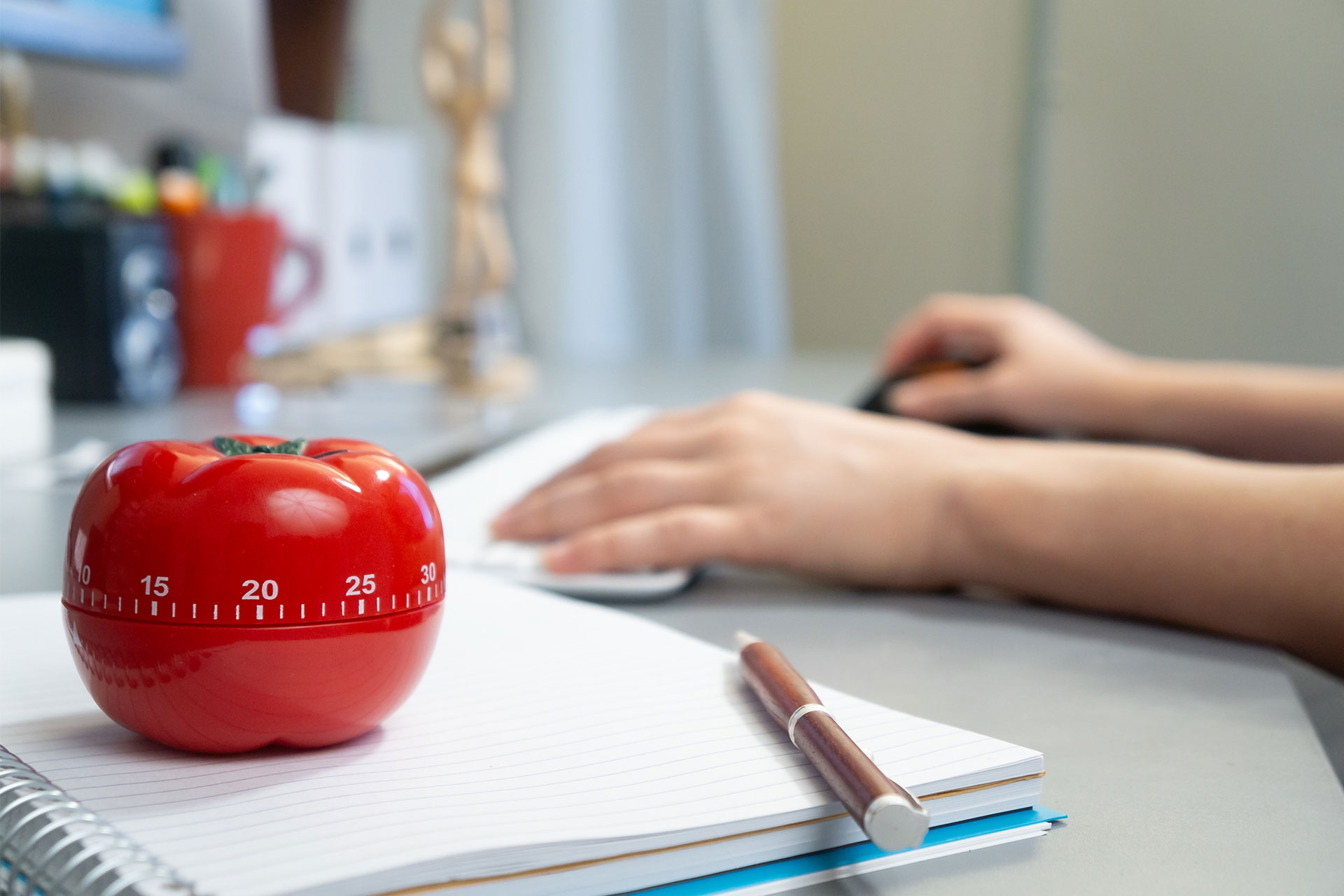 Una persona intenta a lavorare su un'attività con un timer da cucina a forma di pomodoro sulla scrivania