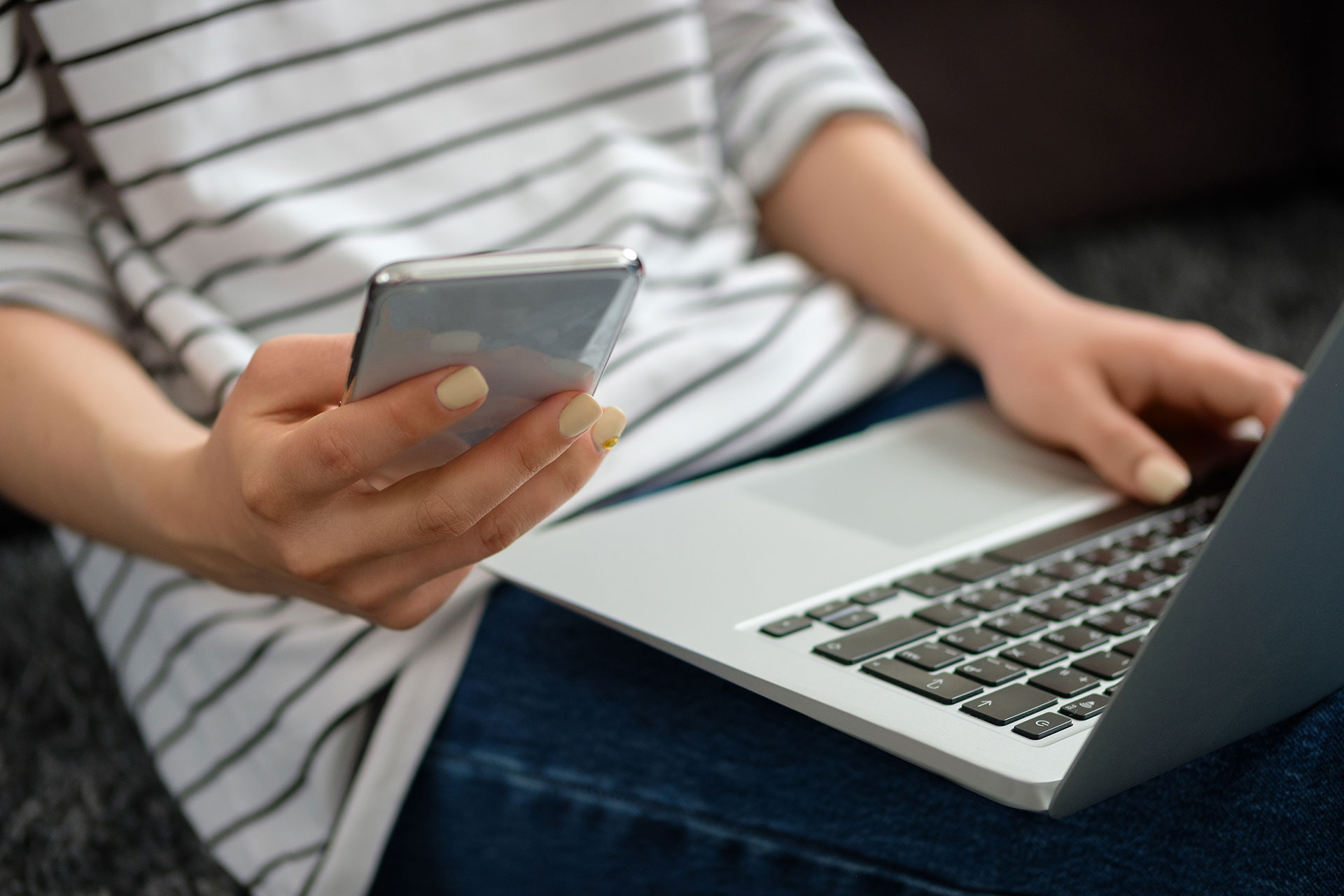 Osoba pracująca na laptopie i trzymająca jednocześnie telefon komórkowy