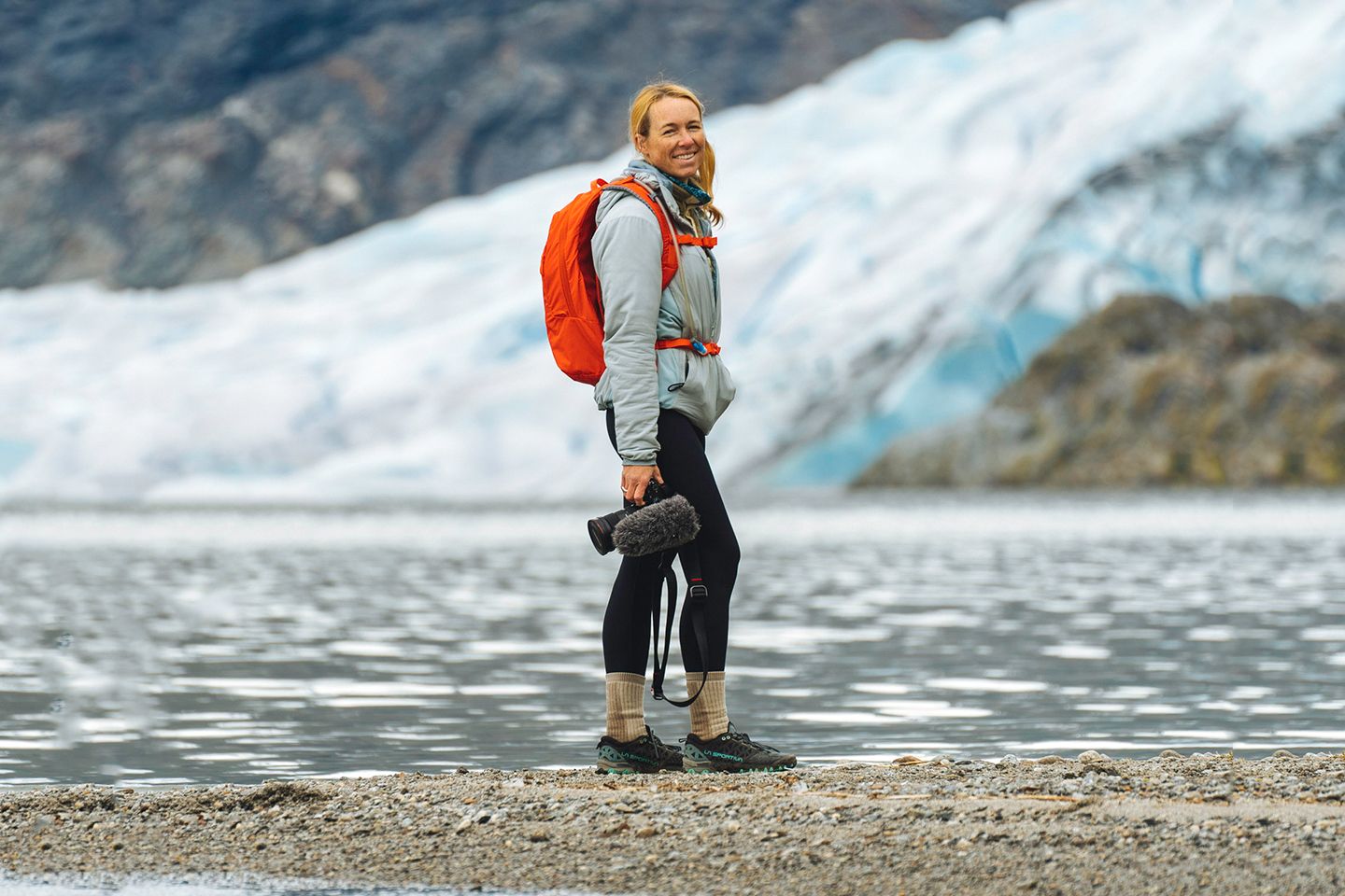 Una mujer de pie frente a un lago sosteniendo una cámara.