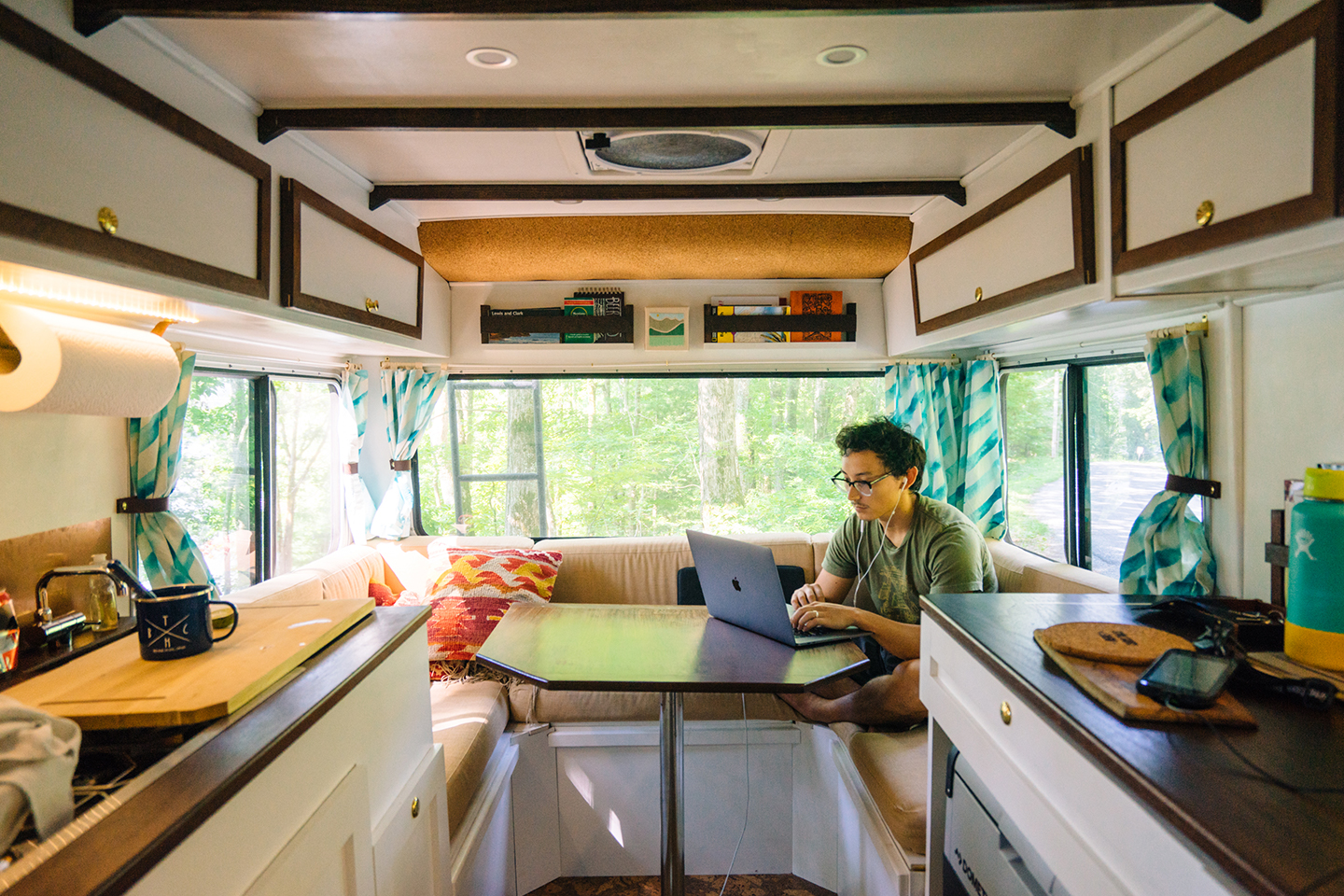 A man sits inside a camper van and works on his laptop.