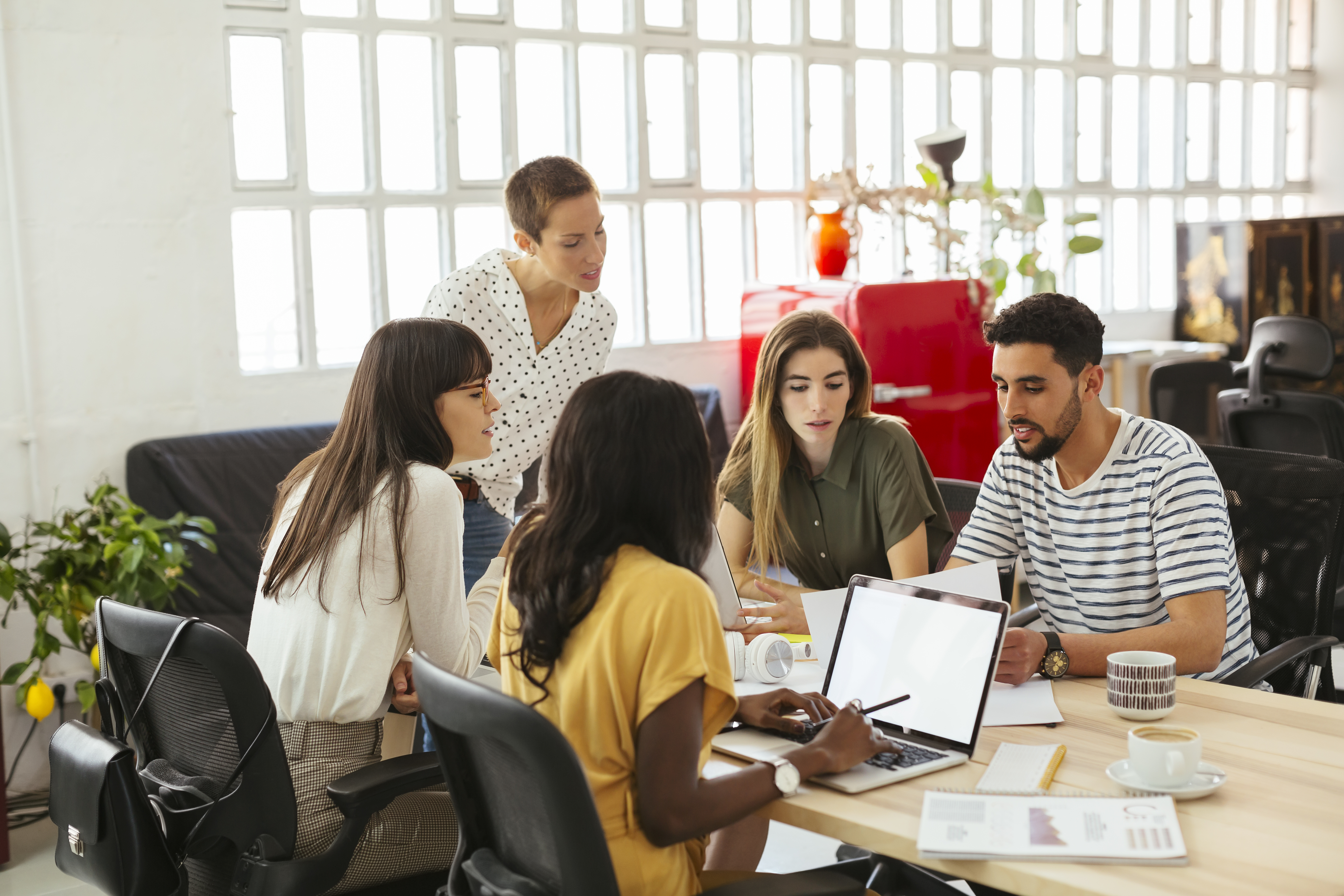 A group of people gather around a laptop in their physical office.