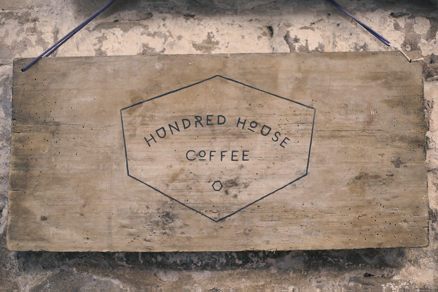 Logo de Hundred House Coffee en una placa de madera.