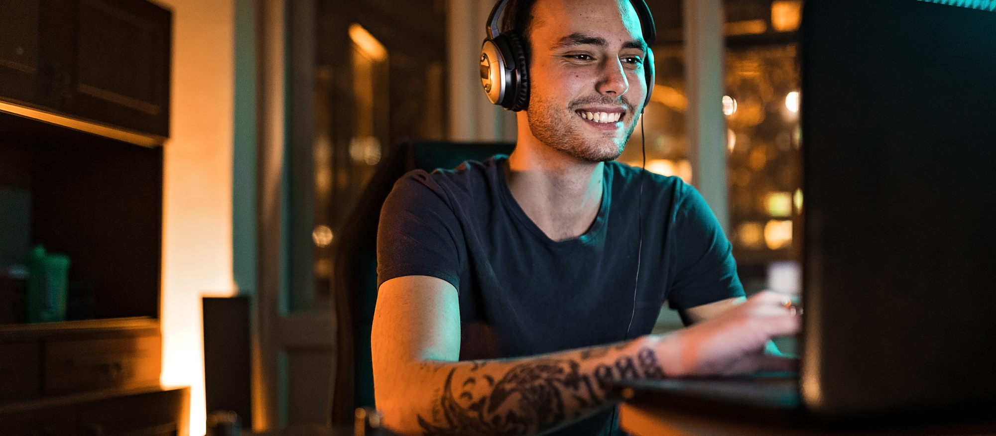 A man with headphones smiles at his computer screen