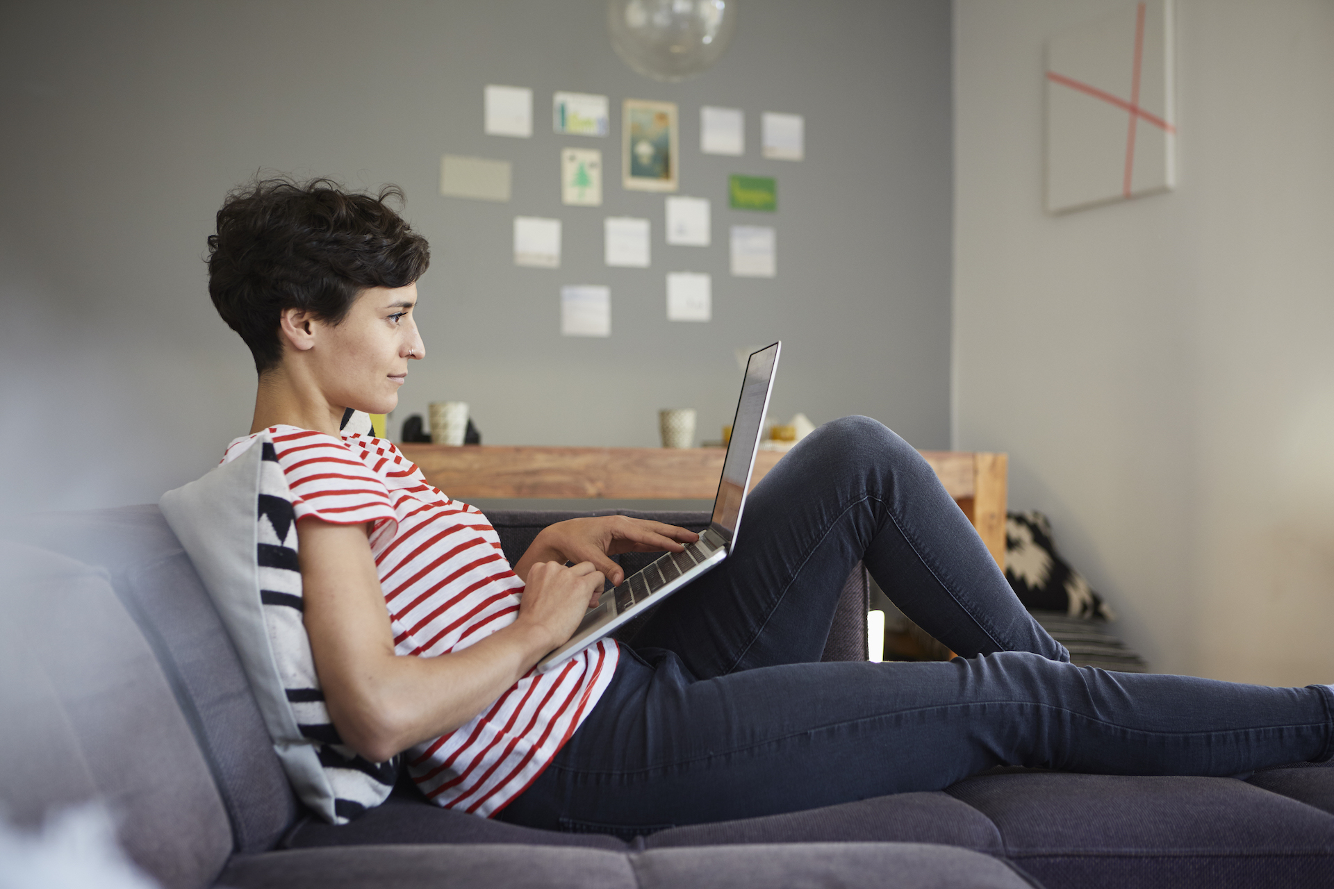 Femme télétravaillant sur son ordinateur portable tout en étant confortablement installée sur son canapé