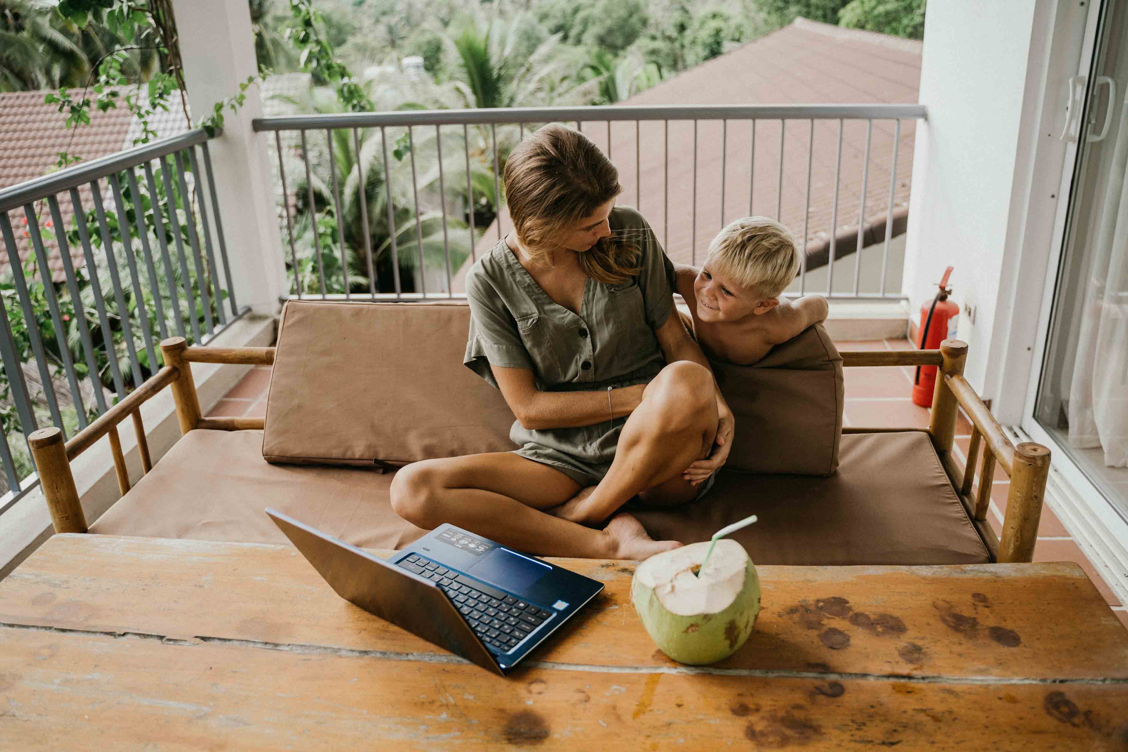 Une mère assise sur un balcon en face de son enfant fait du télétravail sur son ordinateur portable