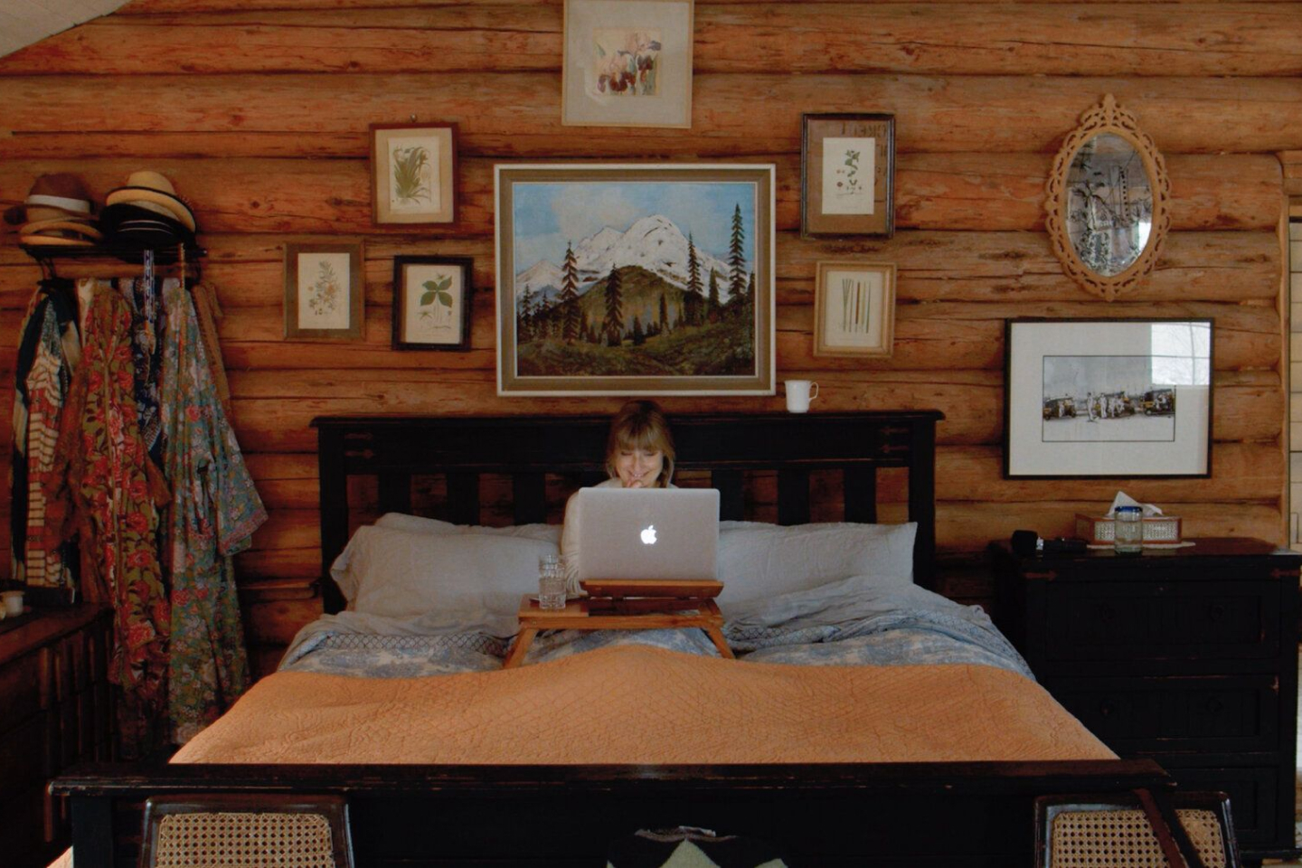 A person working on a MacBook while in bed in a wood paneled room.