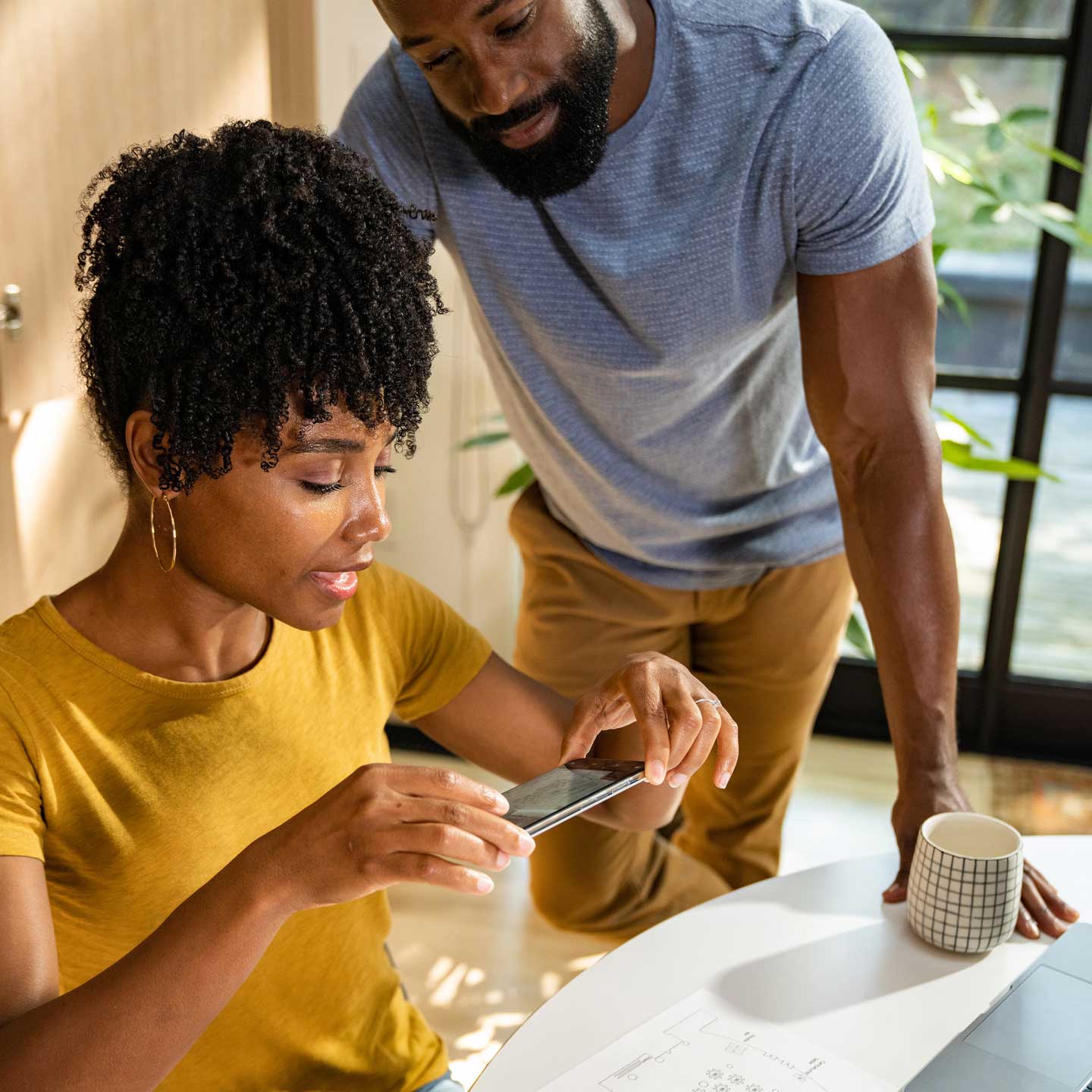 Woman sitting at desk scanning document with phone with man standing next to her