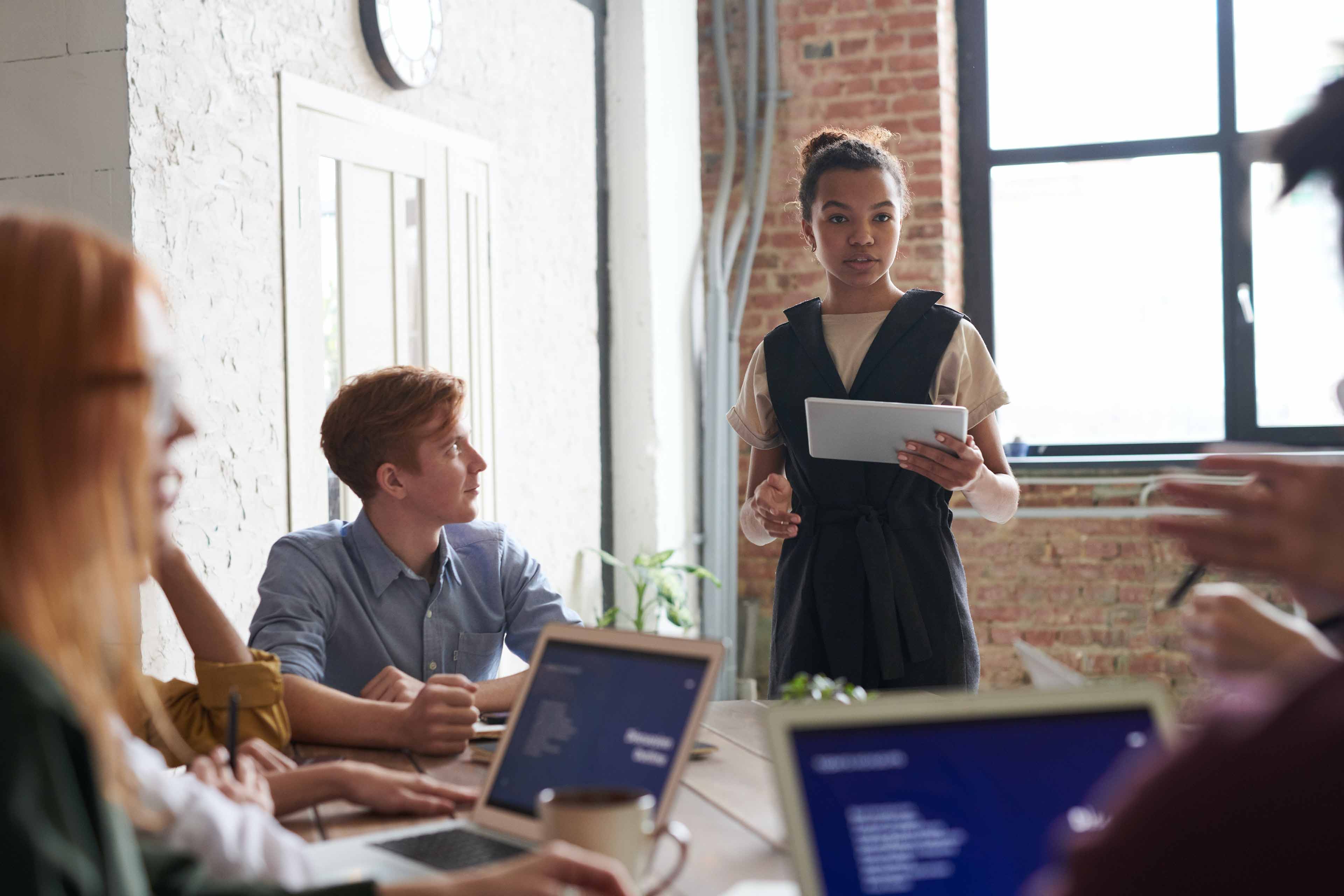 A team sits around a desk and faces someone who delegates tasks to them