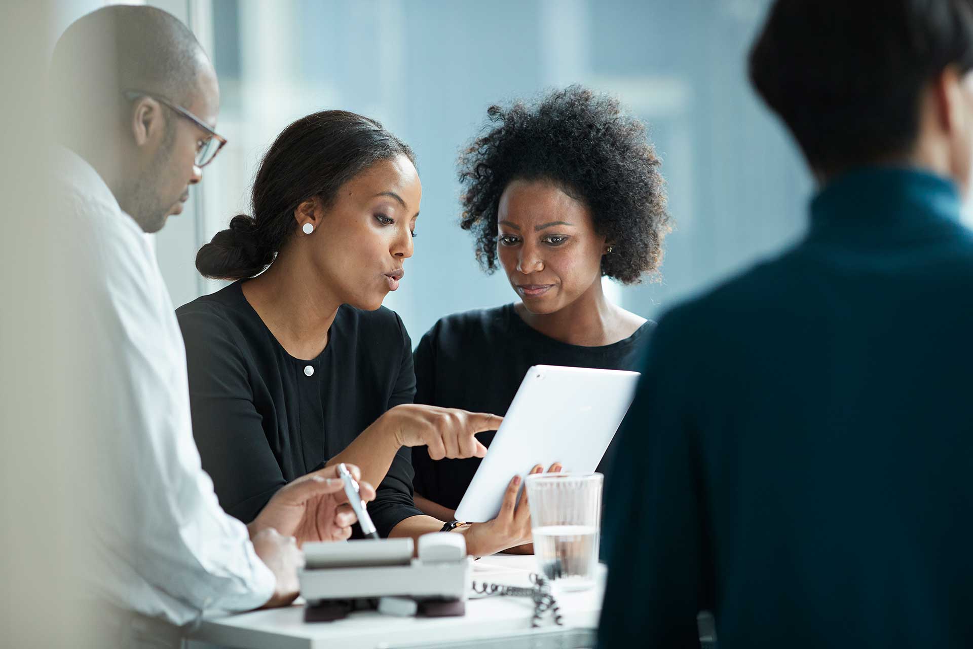 Woman in business setting pointing at tablet as another woman looks at screen