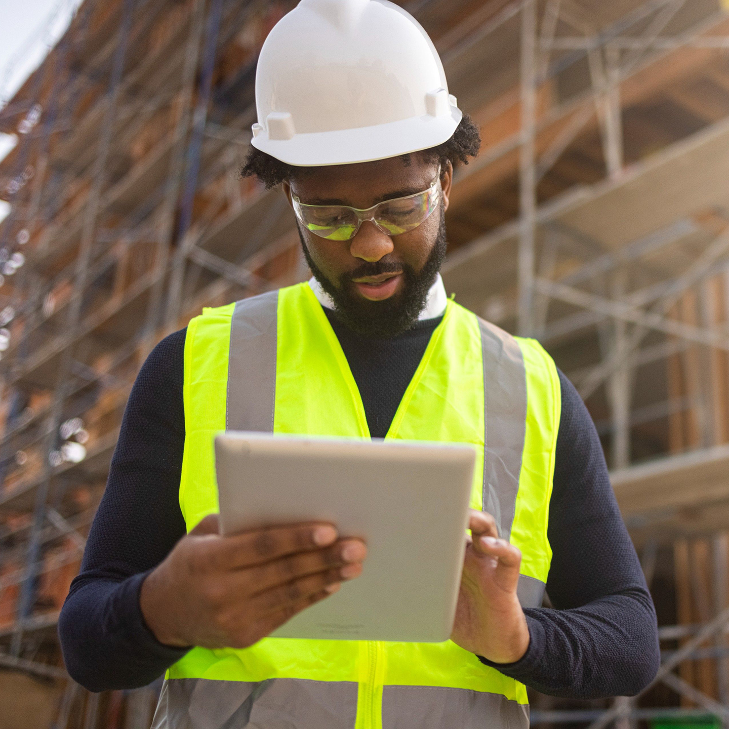 Trabajador de la construcción sosteniendo una <em>tablet</em> delante de una obra