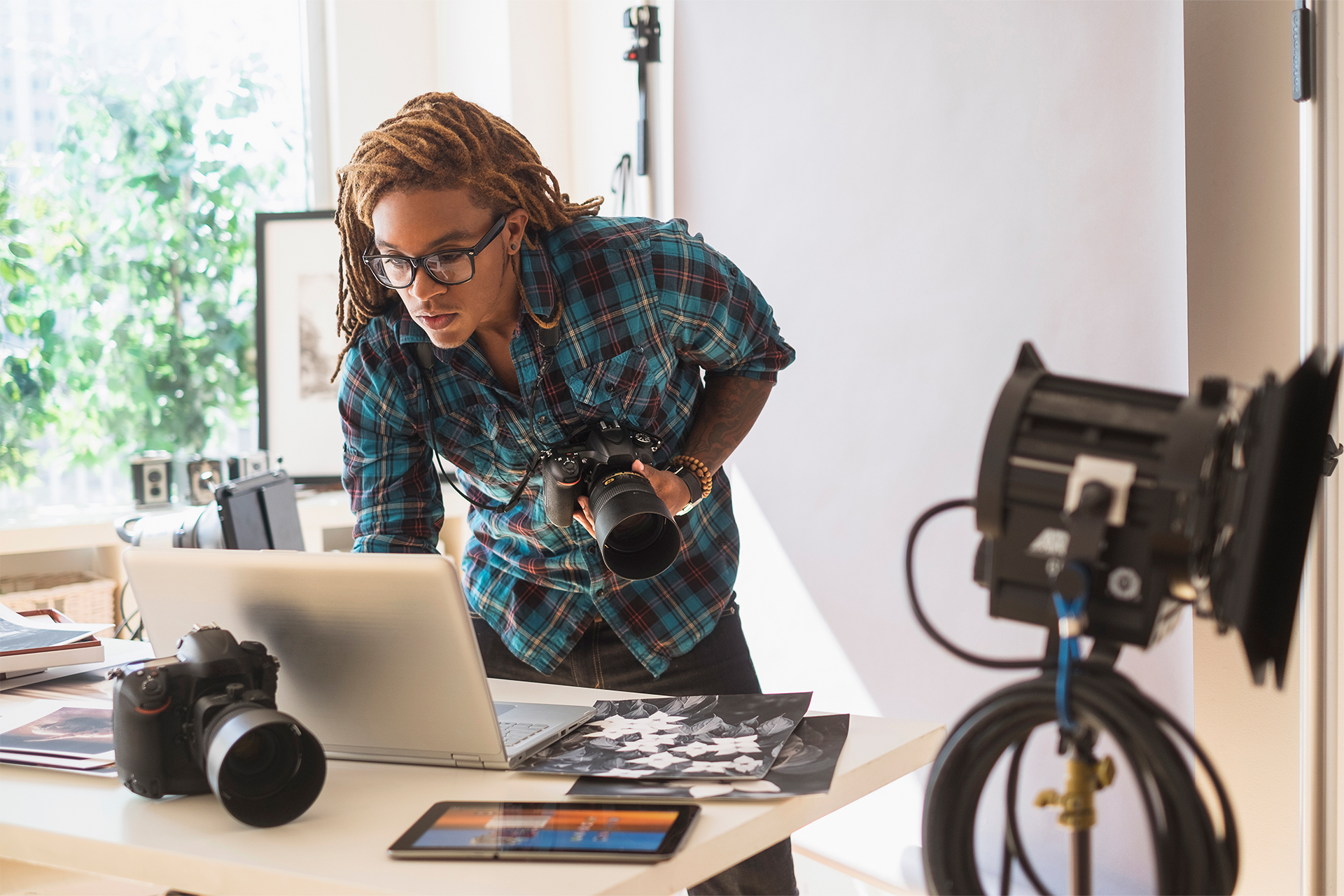 hombre en un estudio de fotografía se inclina sobre una computadora portátil mientras sostiene la cámara