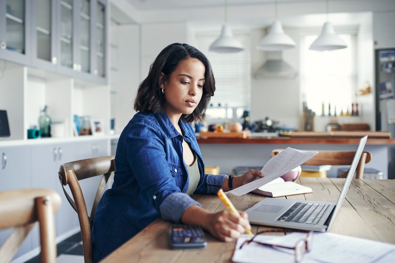 A professional works at a laptop while also writing something on paper.