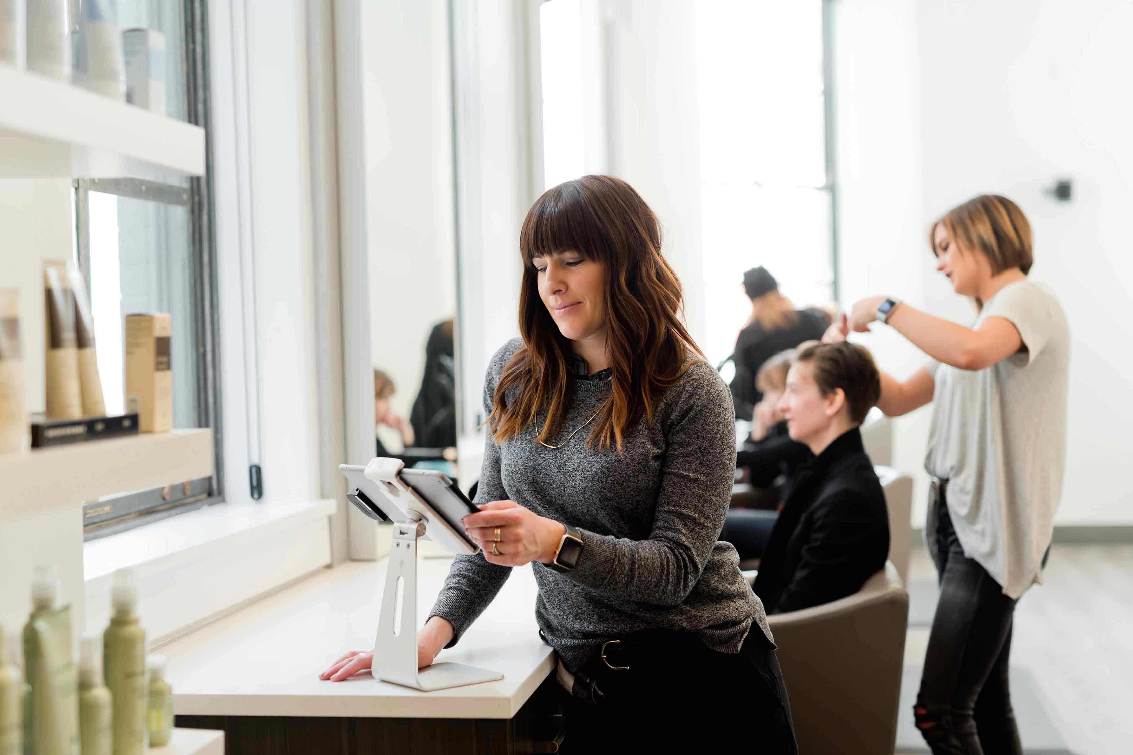 Someone in a hair salon uses a touchscreen mobile device to grow their small business