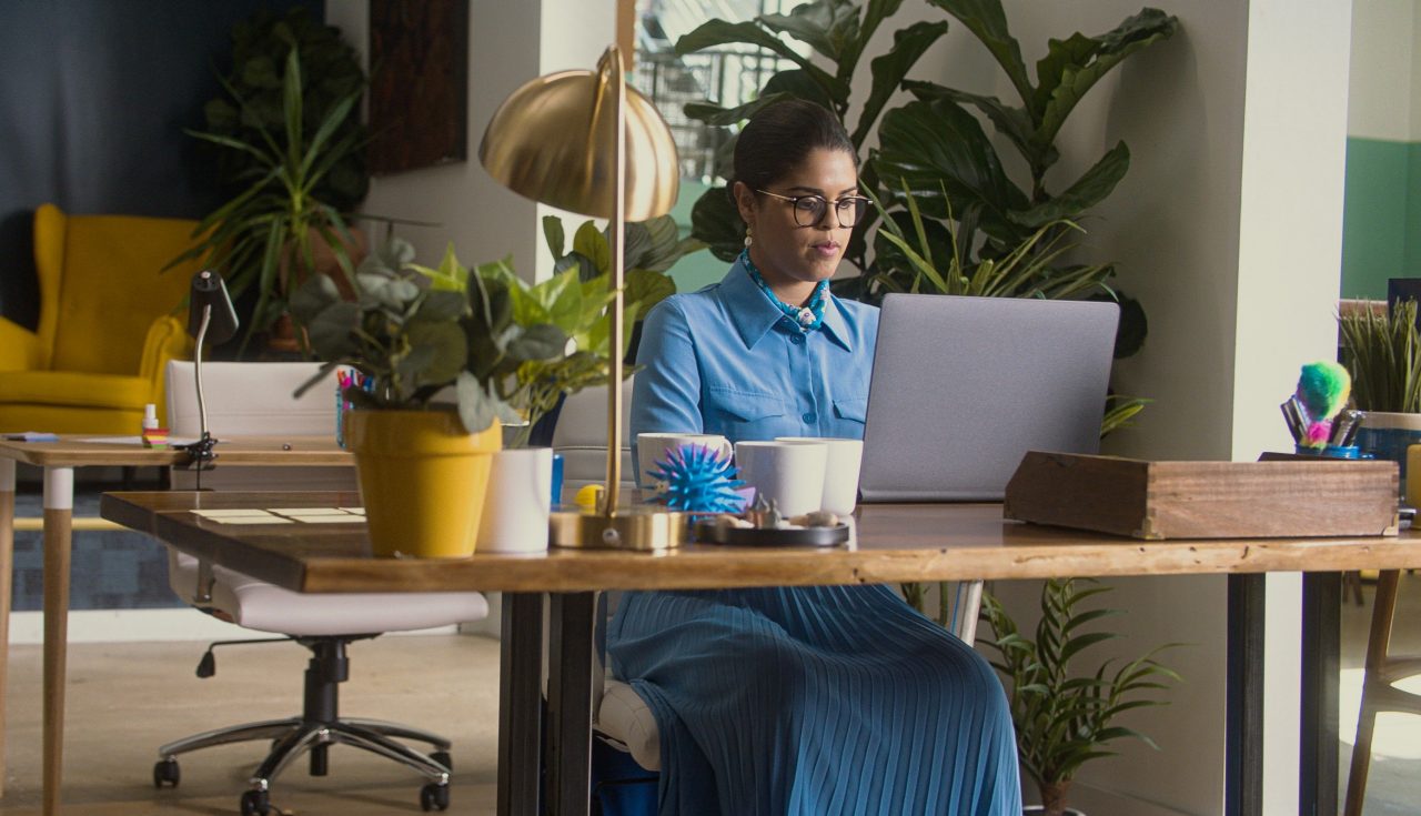 Seorang wanita yang mengerjakan laptop di mejanya di lingkungan yang penuh warna 
