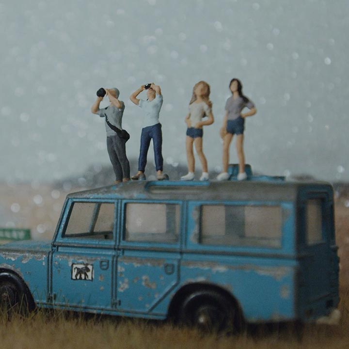 Vier jonge mensen staan op een blauwe wagen en kijken omhoog met verrekijkers 