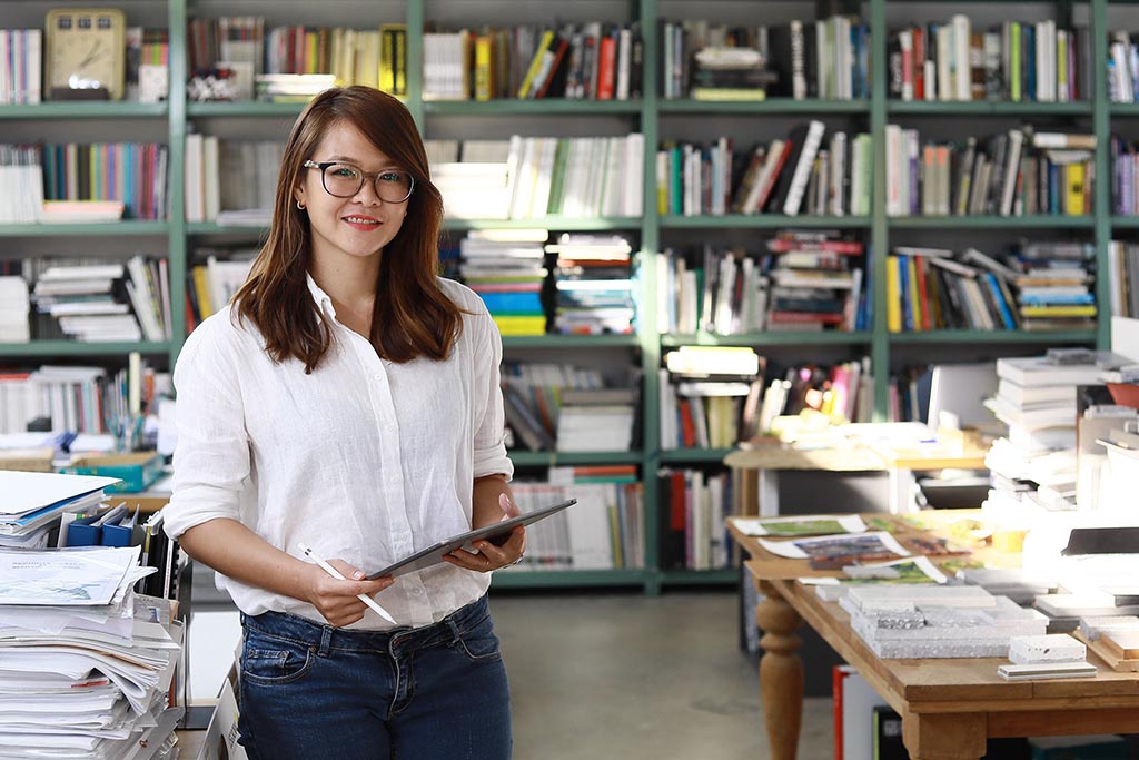 Mujer trabajando con unta tablet frente a estantes llenos de libros y carpetas