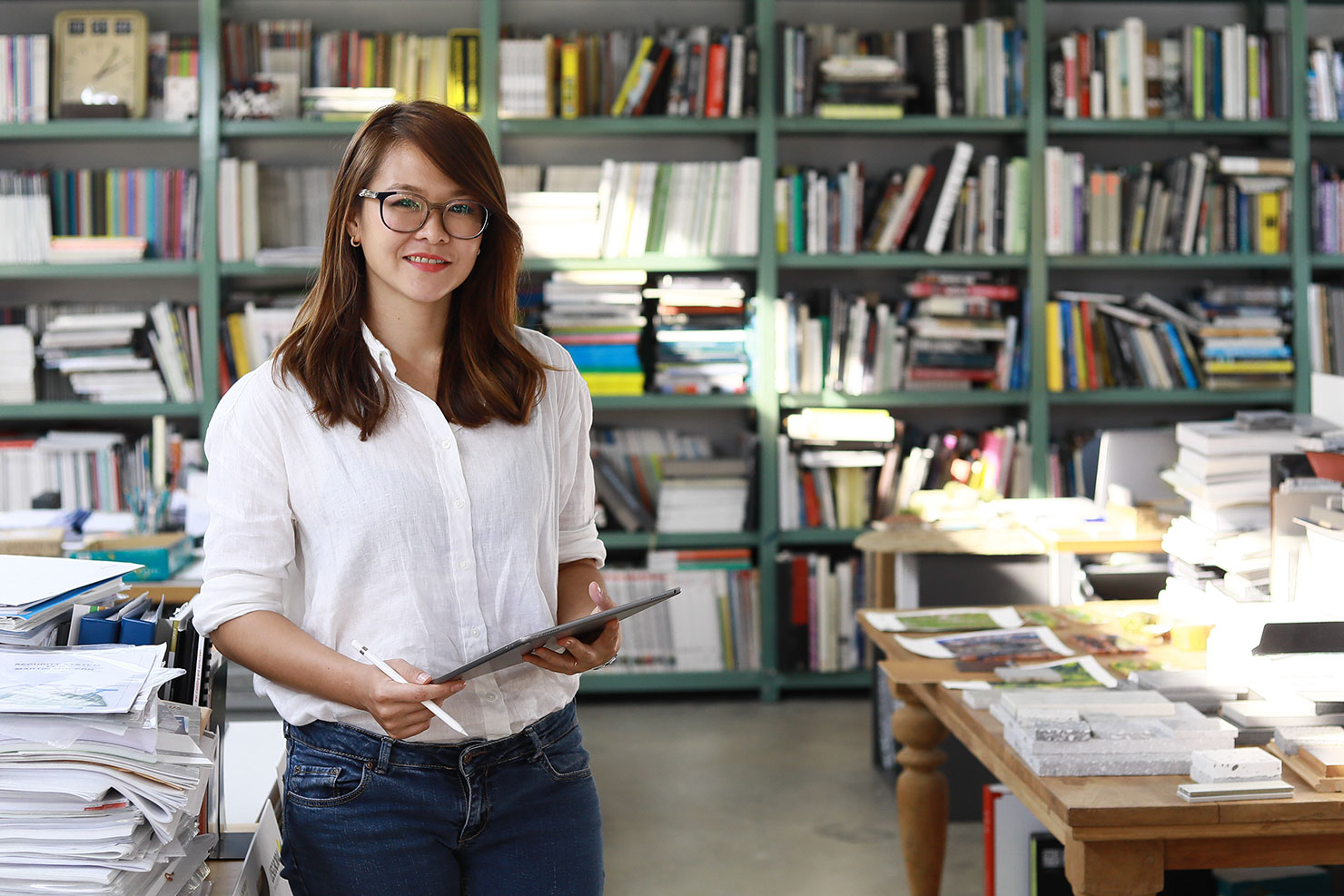 Woman wearing glasses holding a touch pad in front of a shelf full of folders