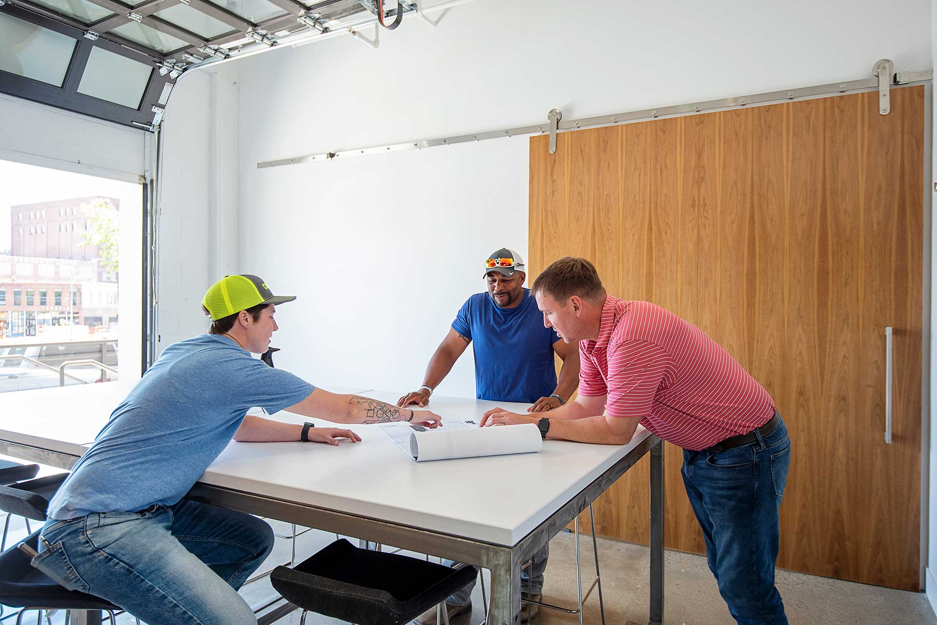3 men stand around table reviewing architectural drawings