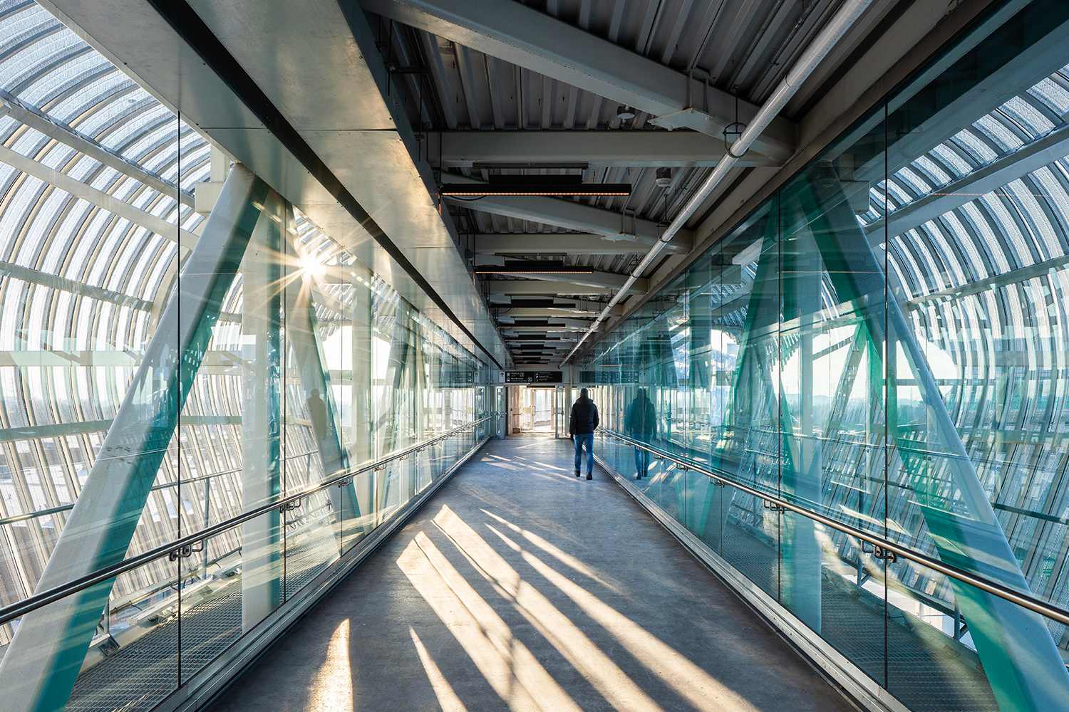 Um homem caminhando em uma ponte de vidro entre edifícios
