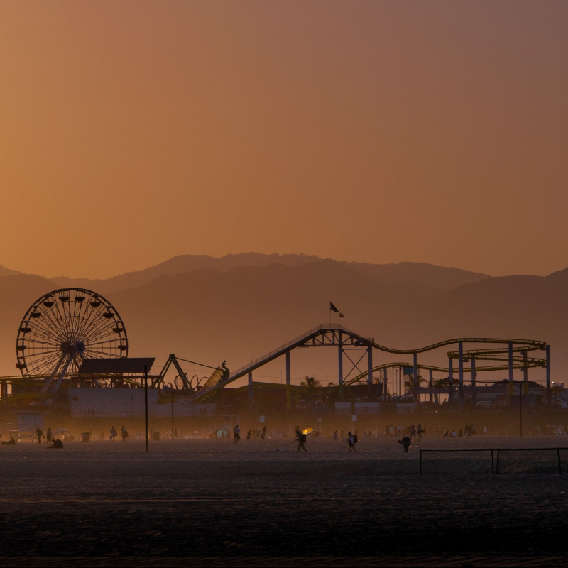 A silhouette of a ferris wheel and roller coaster in front of a mountain range