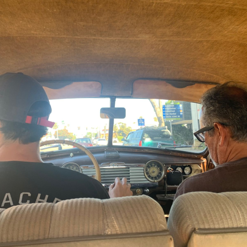 A photo of two men sitting in the front seat of a car, as seen from the point of view of the backseat passenger