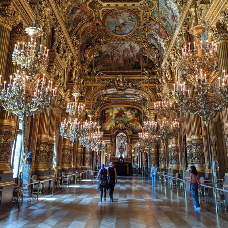 The inside of the Palais Garnier, with gilded walls, a painted ceiling, and large chandeliers