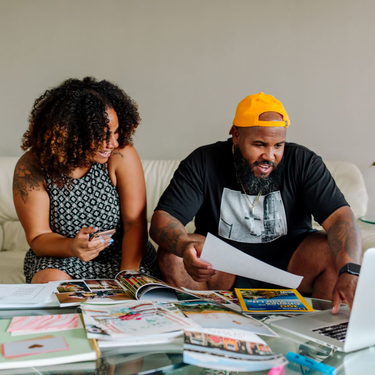 Two people look at a laptop while they flip through magazines.