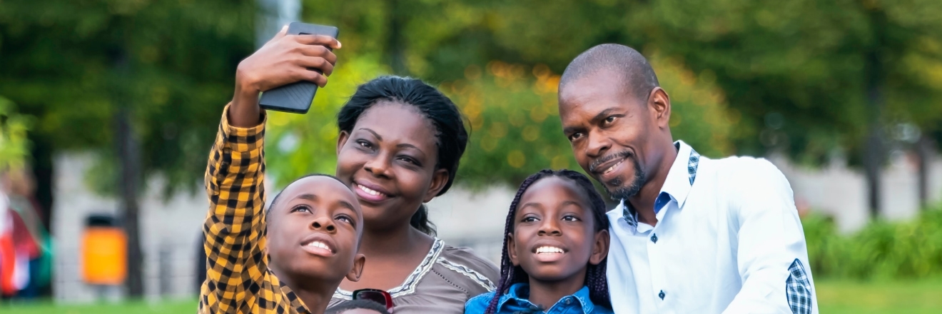 A family pose together while they take a photo with their mobile device.