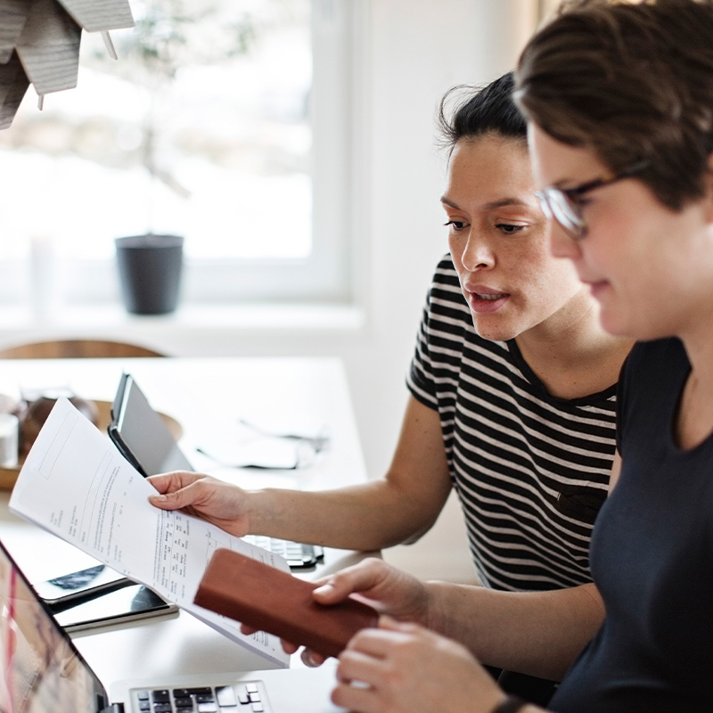 Two people look at paper documents and a computer together