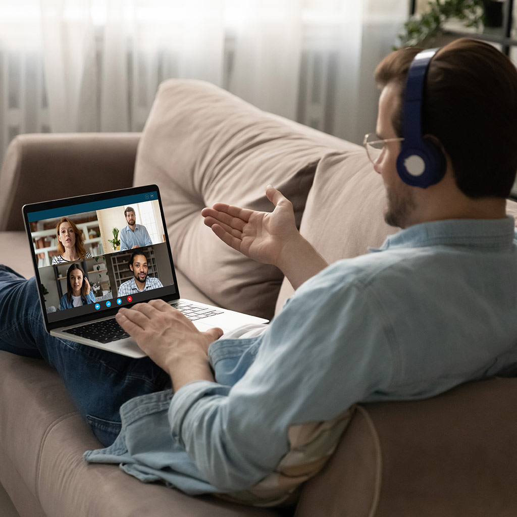Persona sentada en un sofá y participando en una videoconferencia con su portátil