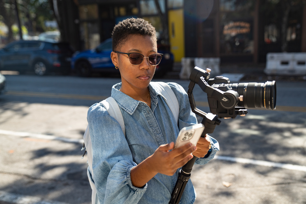 Vrouw die een videocamera vasthoudt en naar een telefoon kijkt