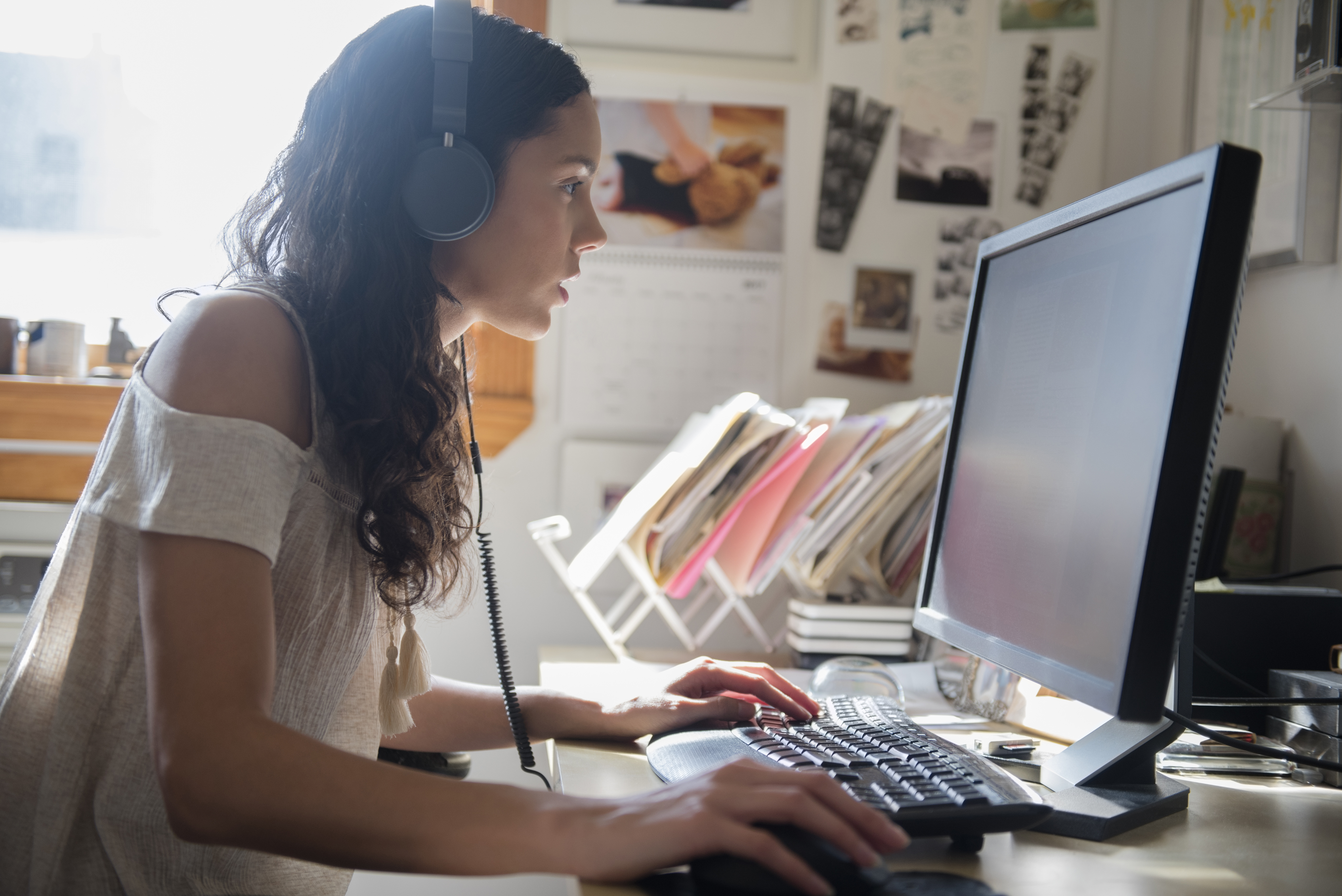 A freelancer translator wears headphones to listen to some audio while looking at their computer screen.