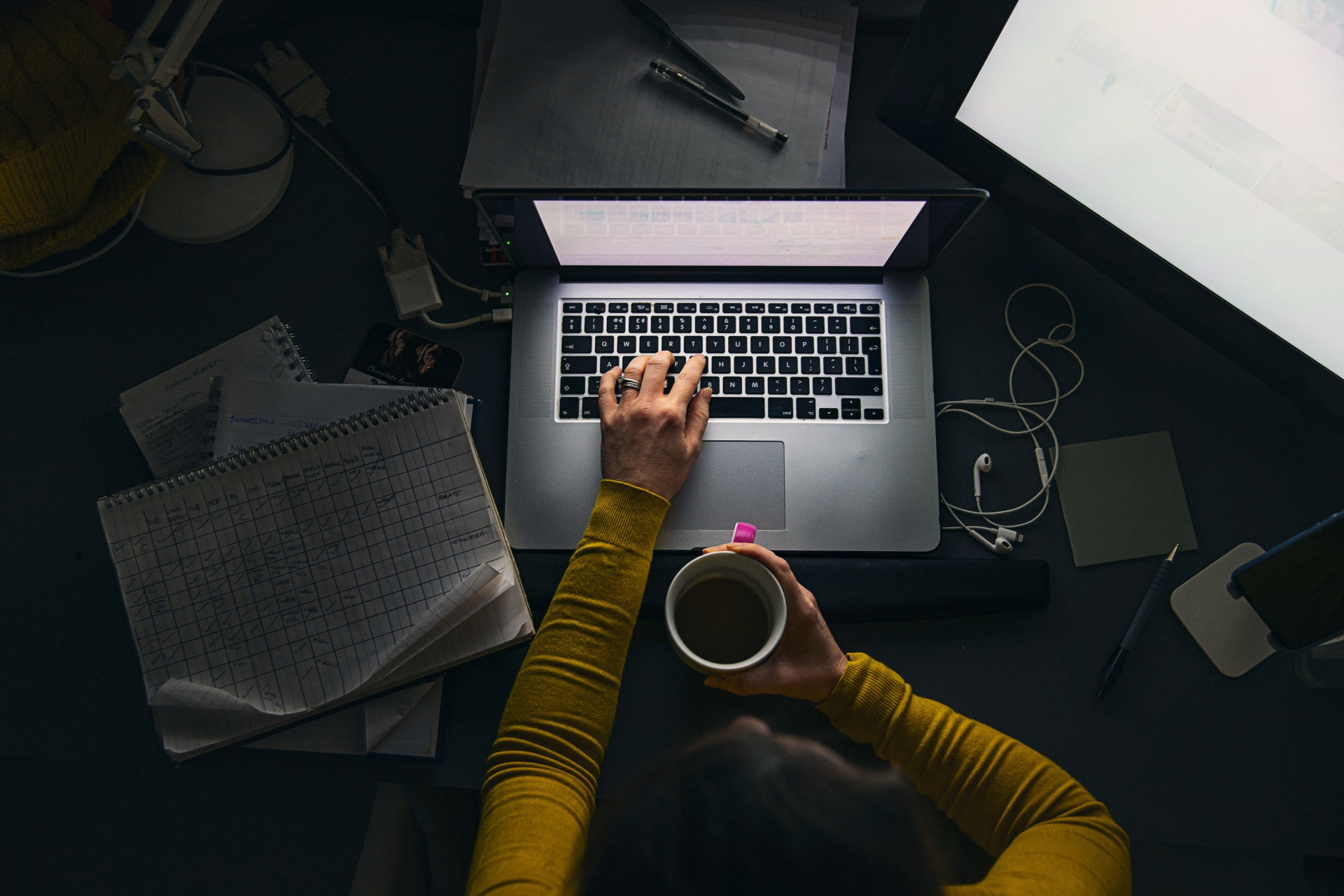 Una persona sentada frente a un escritorio trabajando con un portátil y sosteniendo una taza de café.