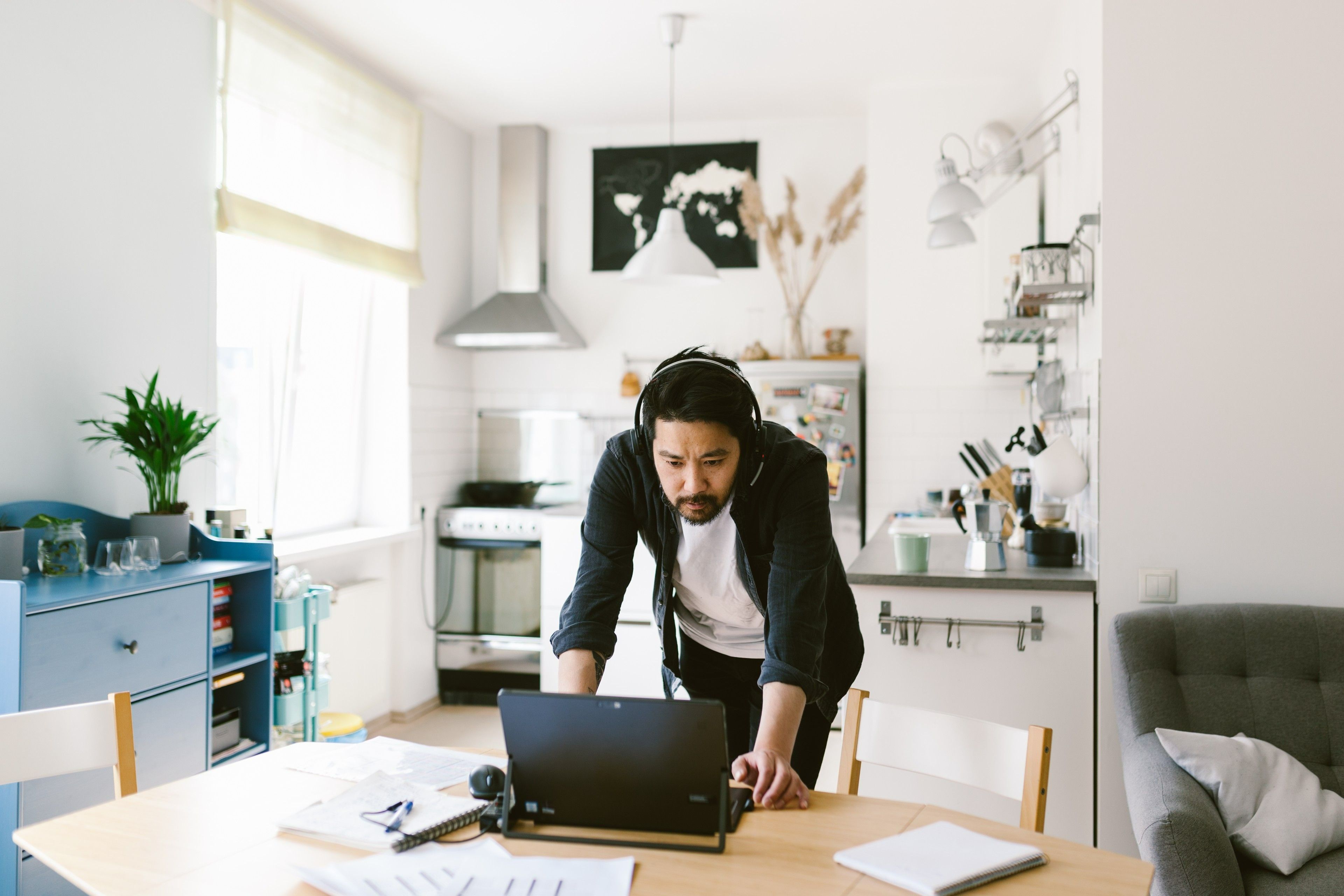 Seorang pekerja jarak jauh menggunakan laptop dan headset untuk berpartisipasi dalam rapat hibrida dari lingkungan kantor rumahnya