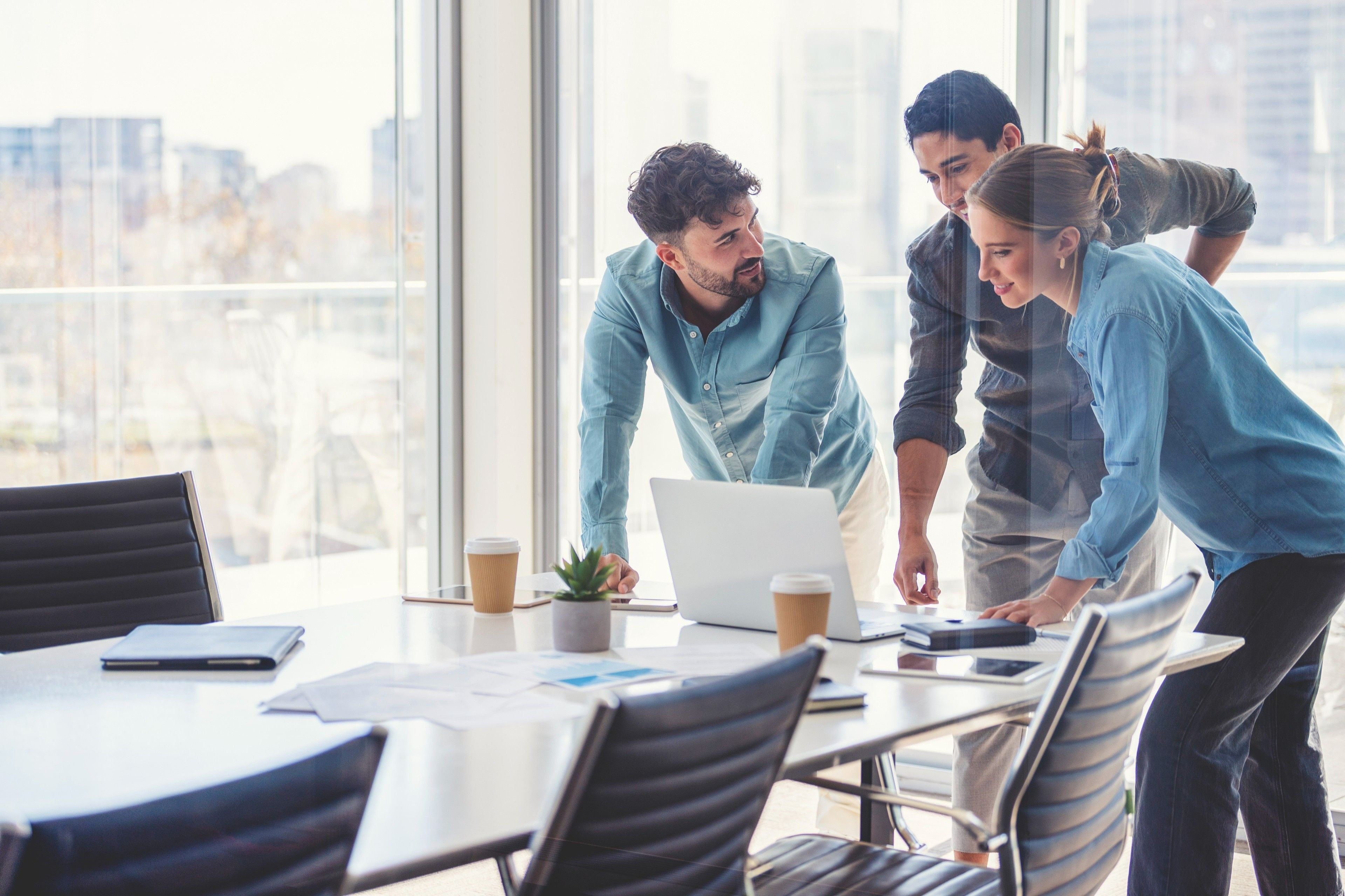 A group of colleagues gather round a laptop to participate in a hybrid meeting