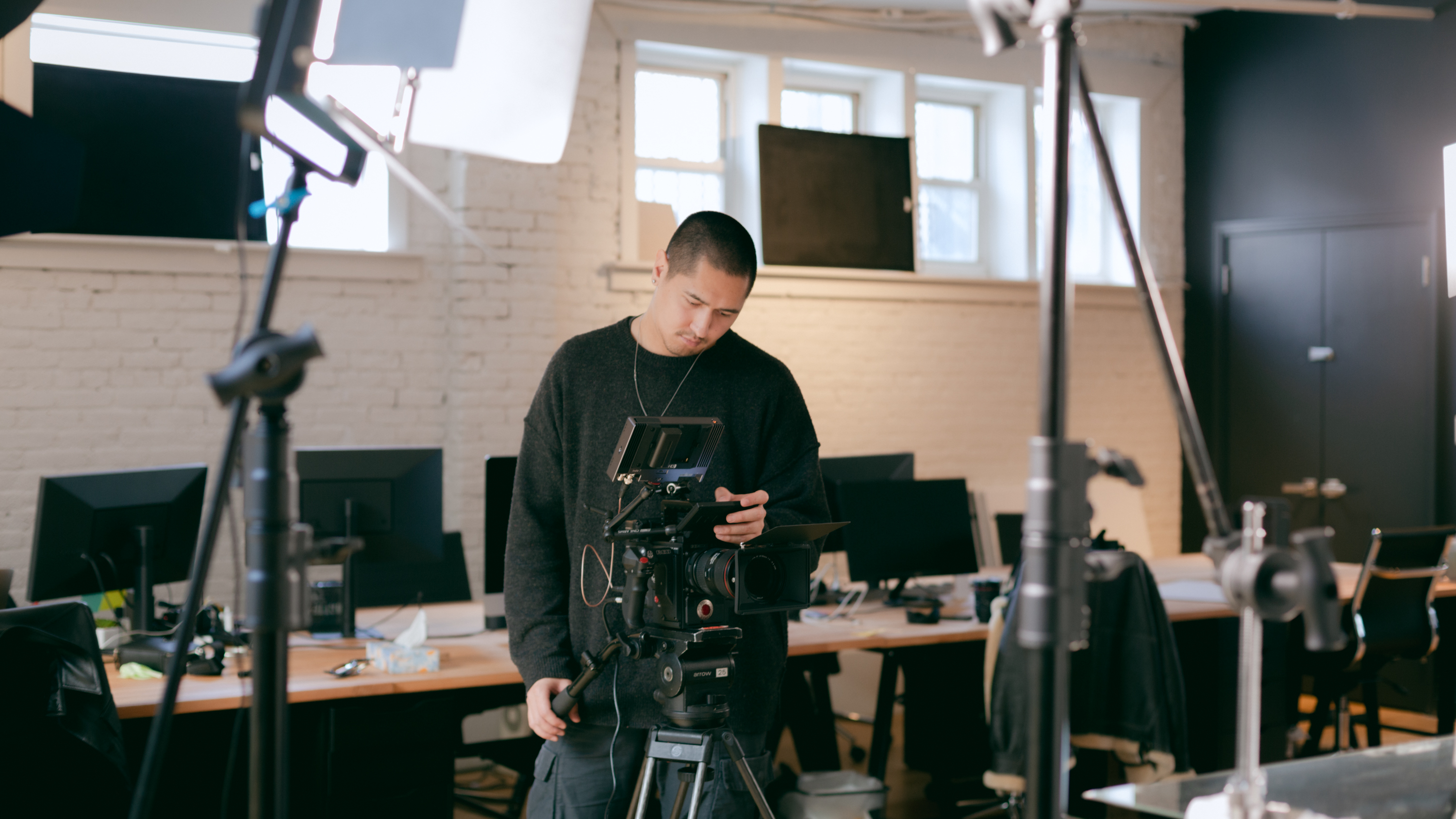 A videographer holds their camera and looks at their footage on the camera monitor.