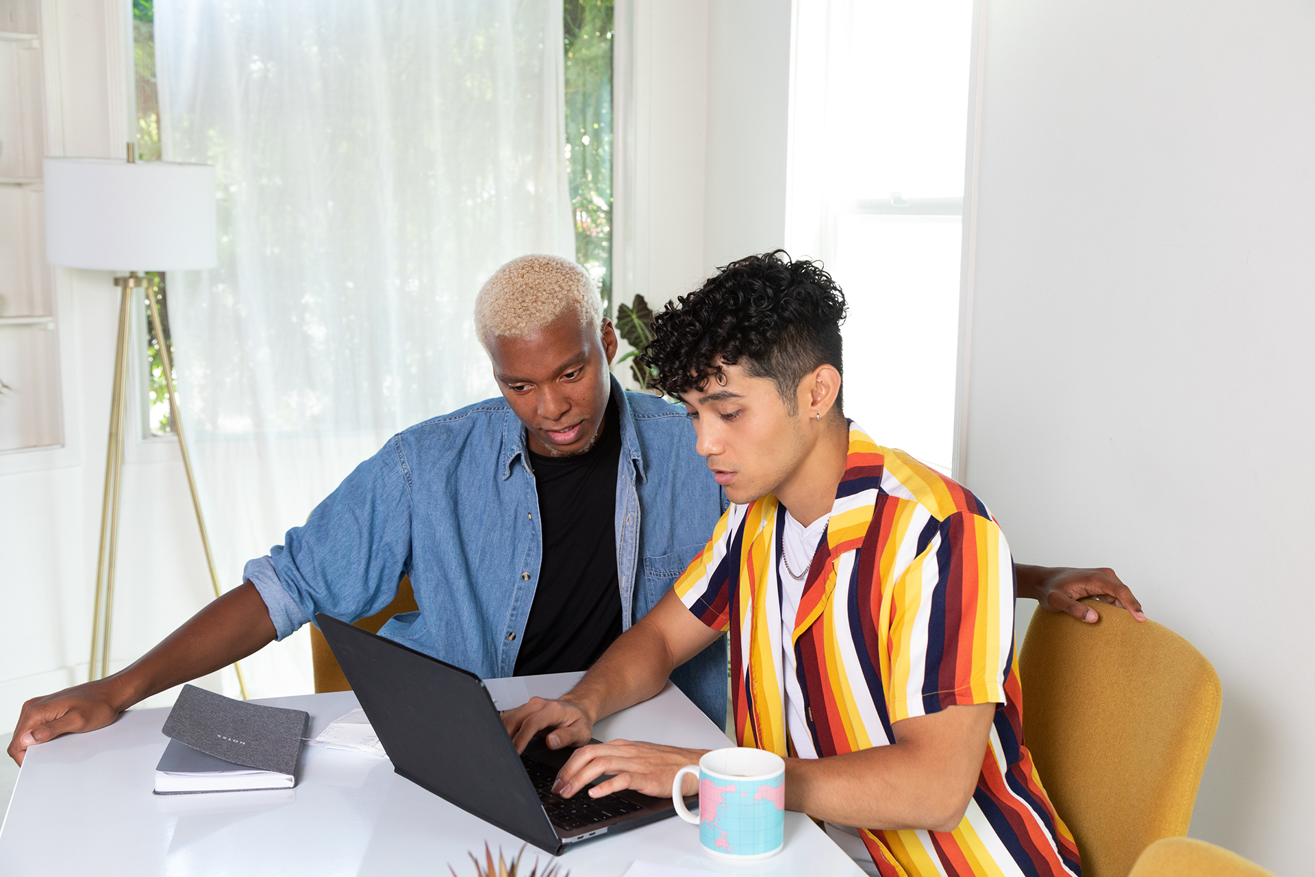 Two people sitting at a table working on a laptop, one person is typing, and the other is observing.