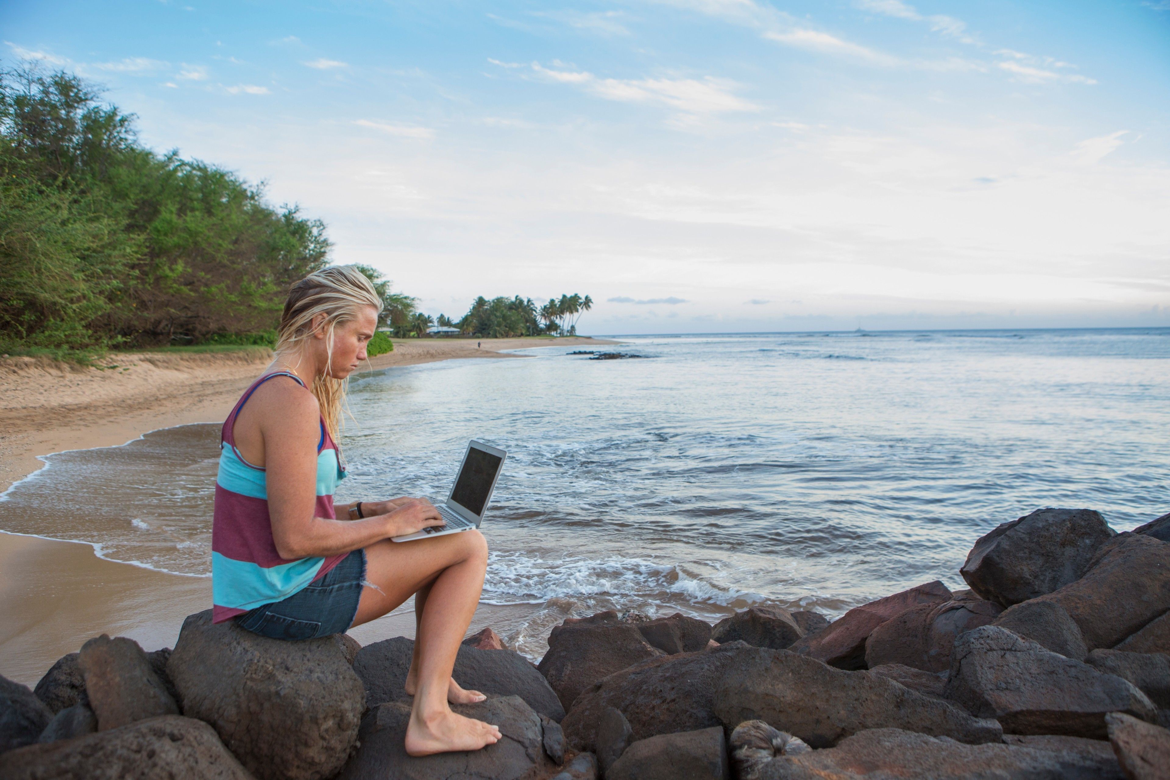 Un'influencer di lifestyle e benessere modifica i suoi contenuti in spiaggia dal suo laptop.