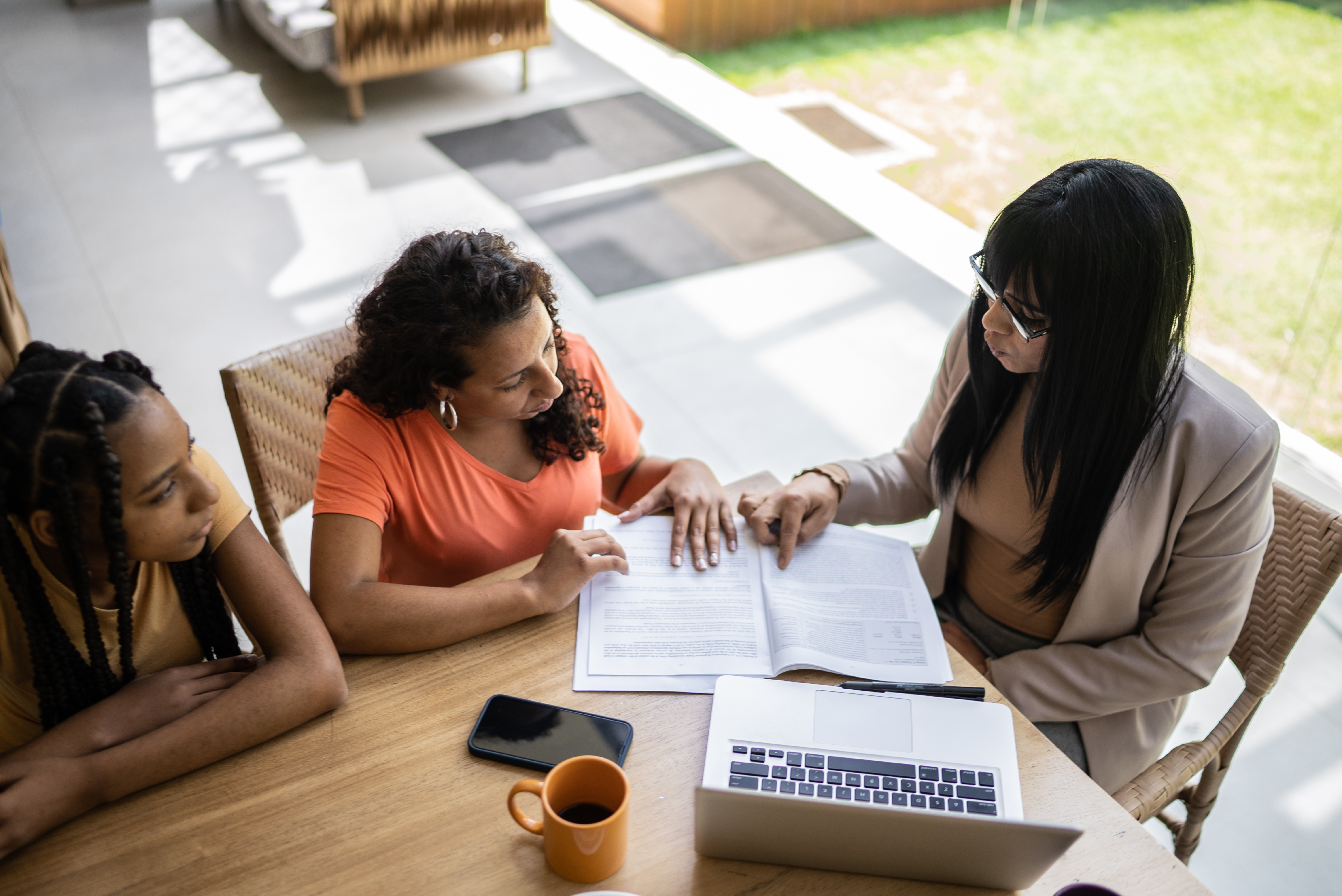 A professional looks over a document with two other people while they sit at a dining room table.