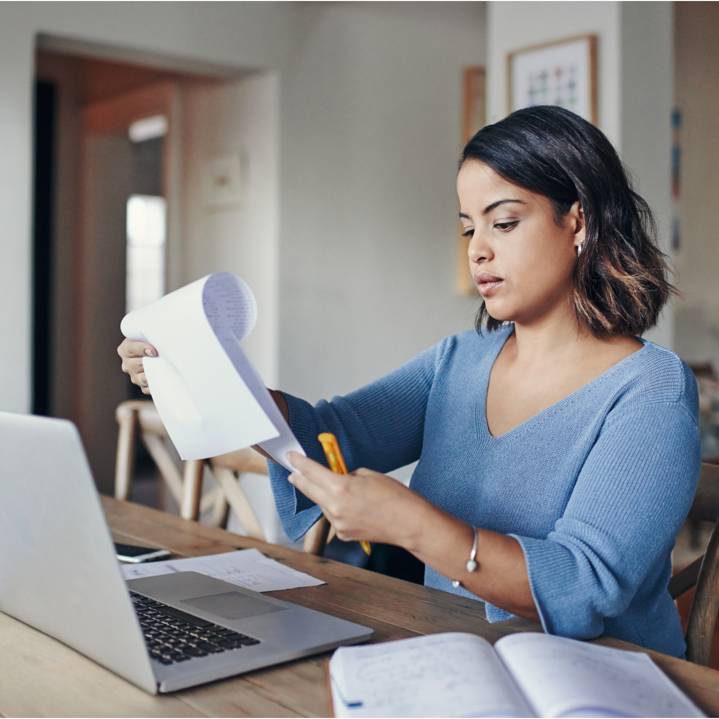 Vrouw die op een laptop werkt en papieren documenten bekijkt.
