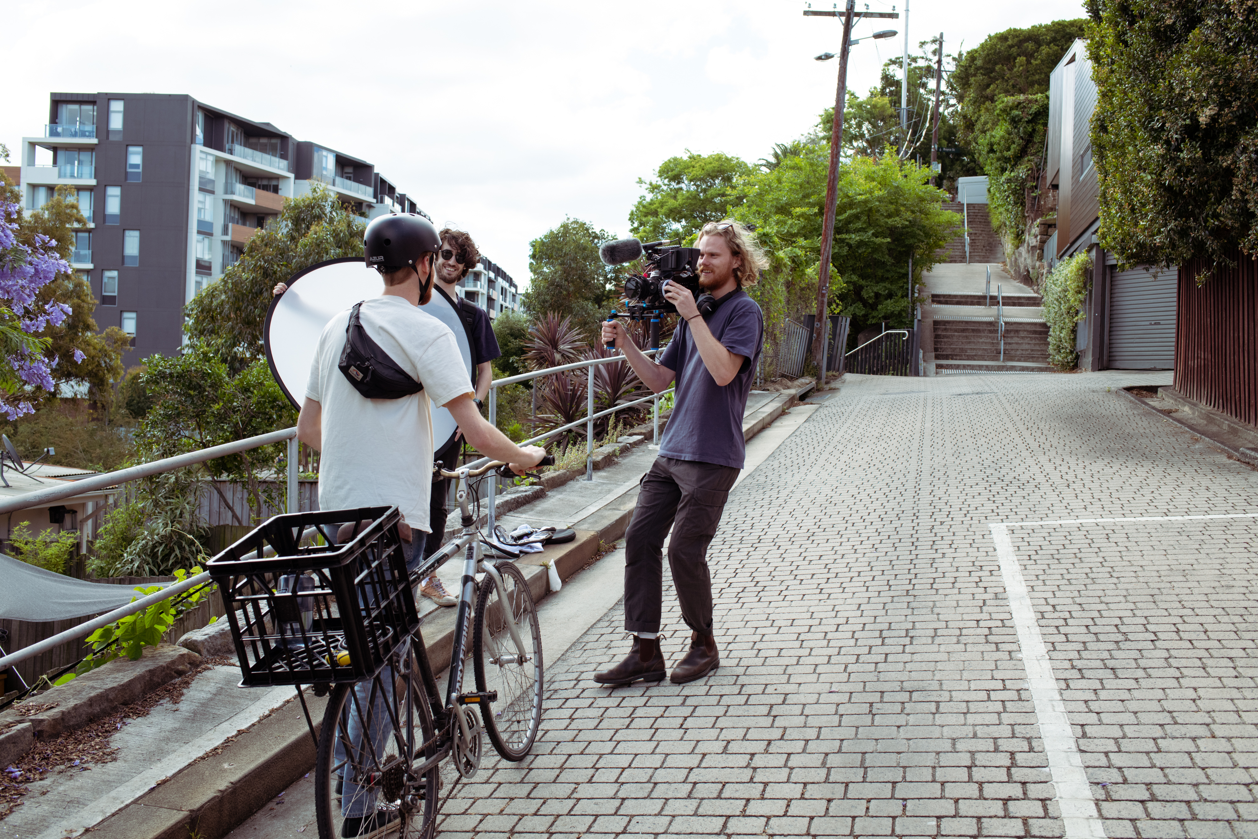 A videographer on set, filming a person walking with a bike.