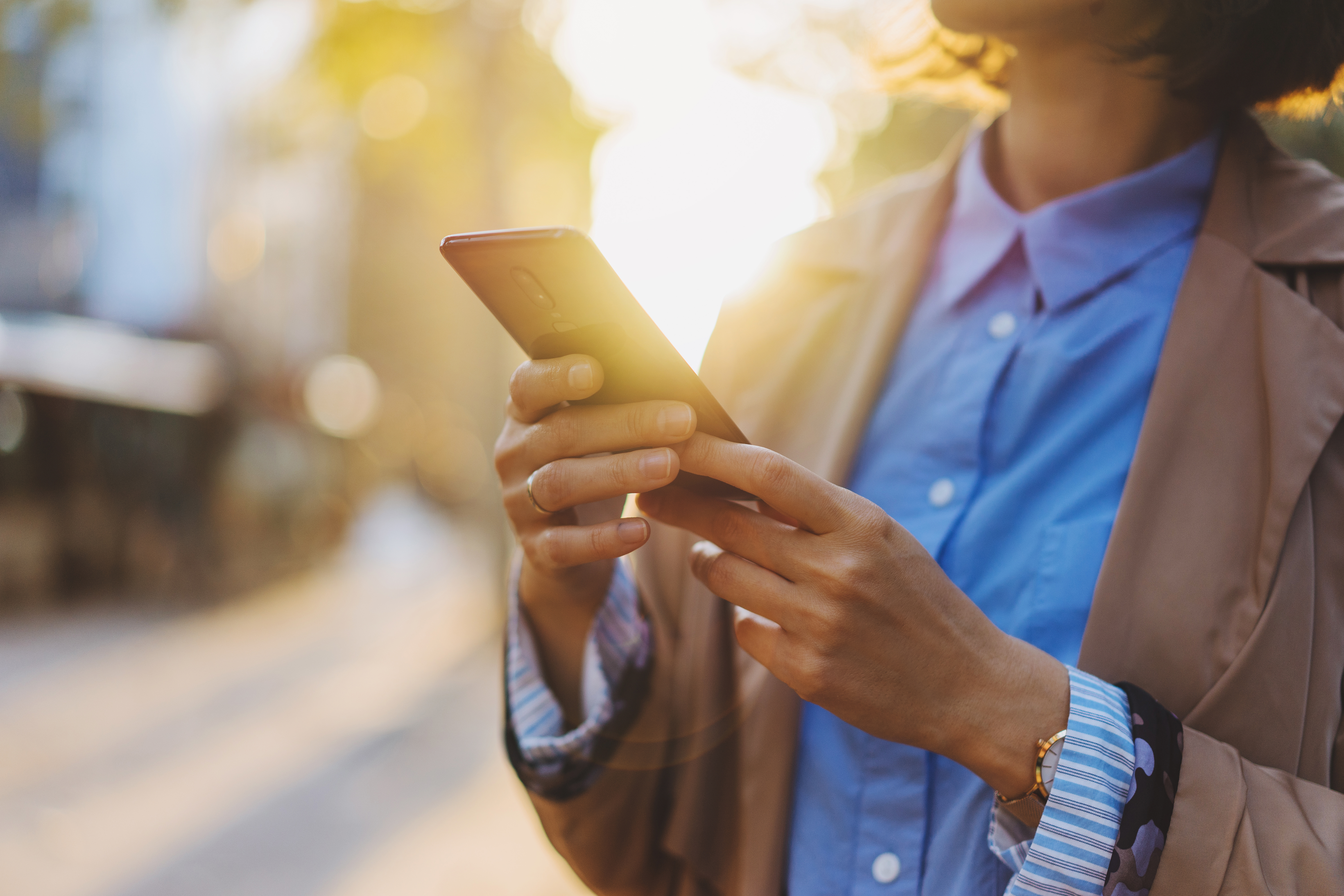 A person looks at their phone while standing on a street.