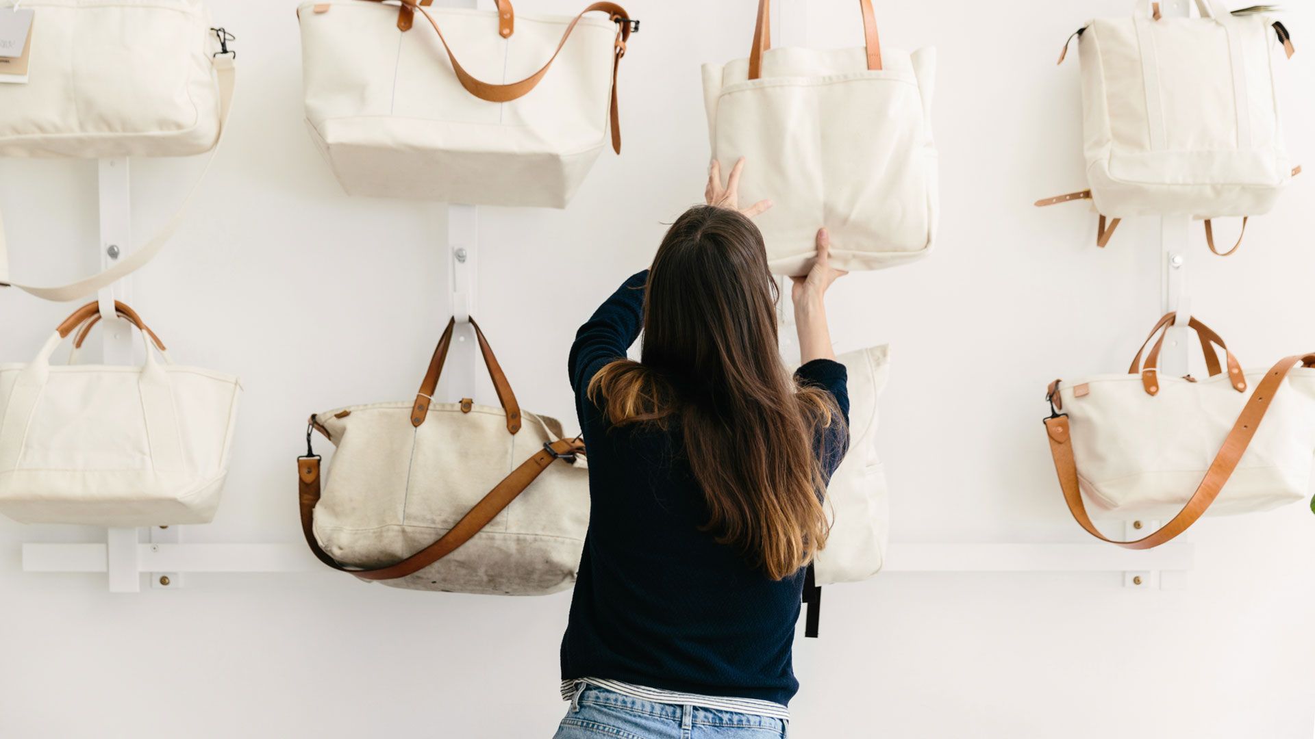 Женщина развешивает белые сумки-шопперы на белой стене