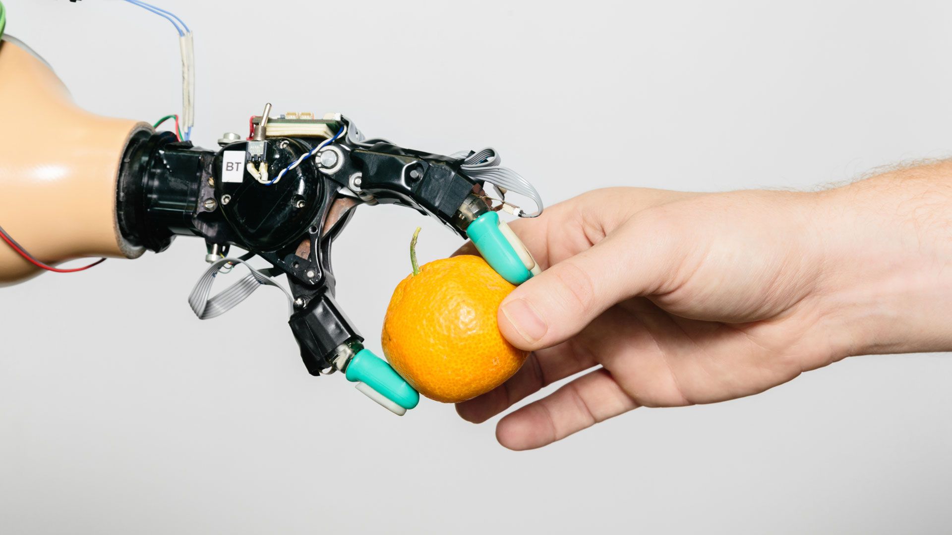 En robothånd, der tager en appelsin fra en menneskelig hånd