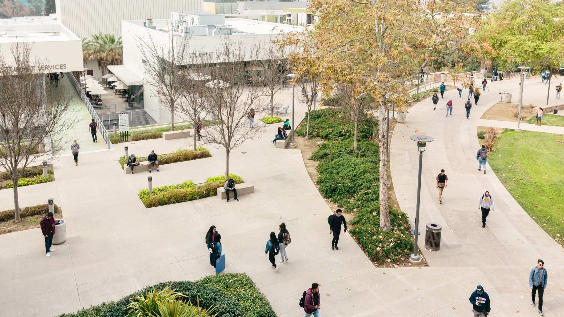 Um campus universitário com espaços verdes e passarelas povoadas por estudantes usando mochilas