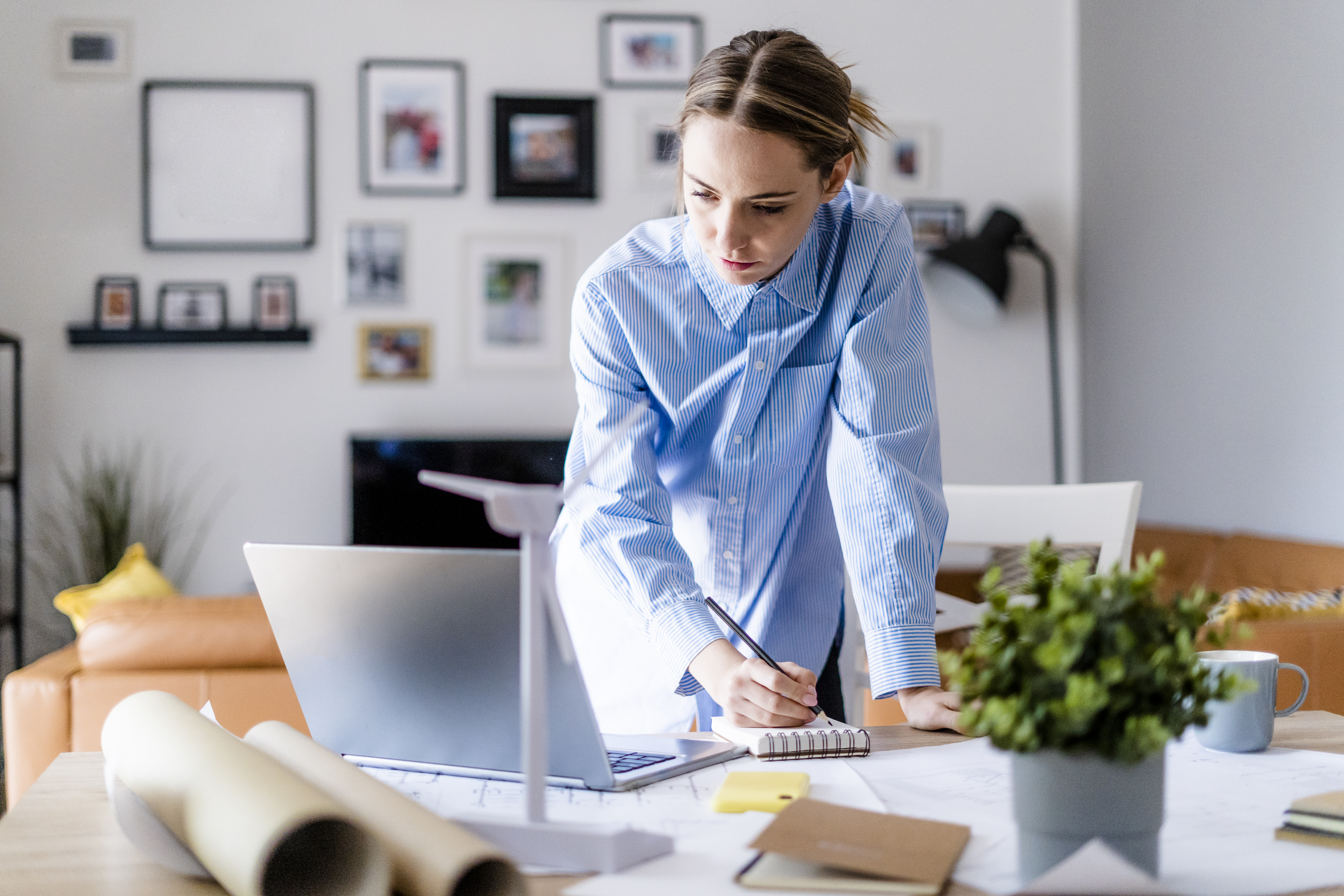 A person writes a list for a writing services invoice while glancing at a file on their laptop.